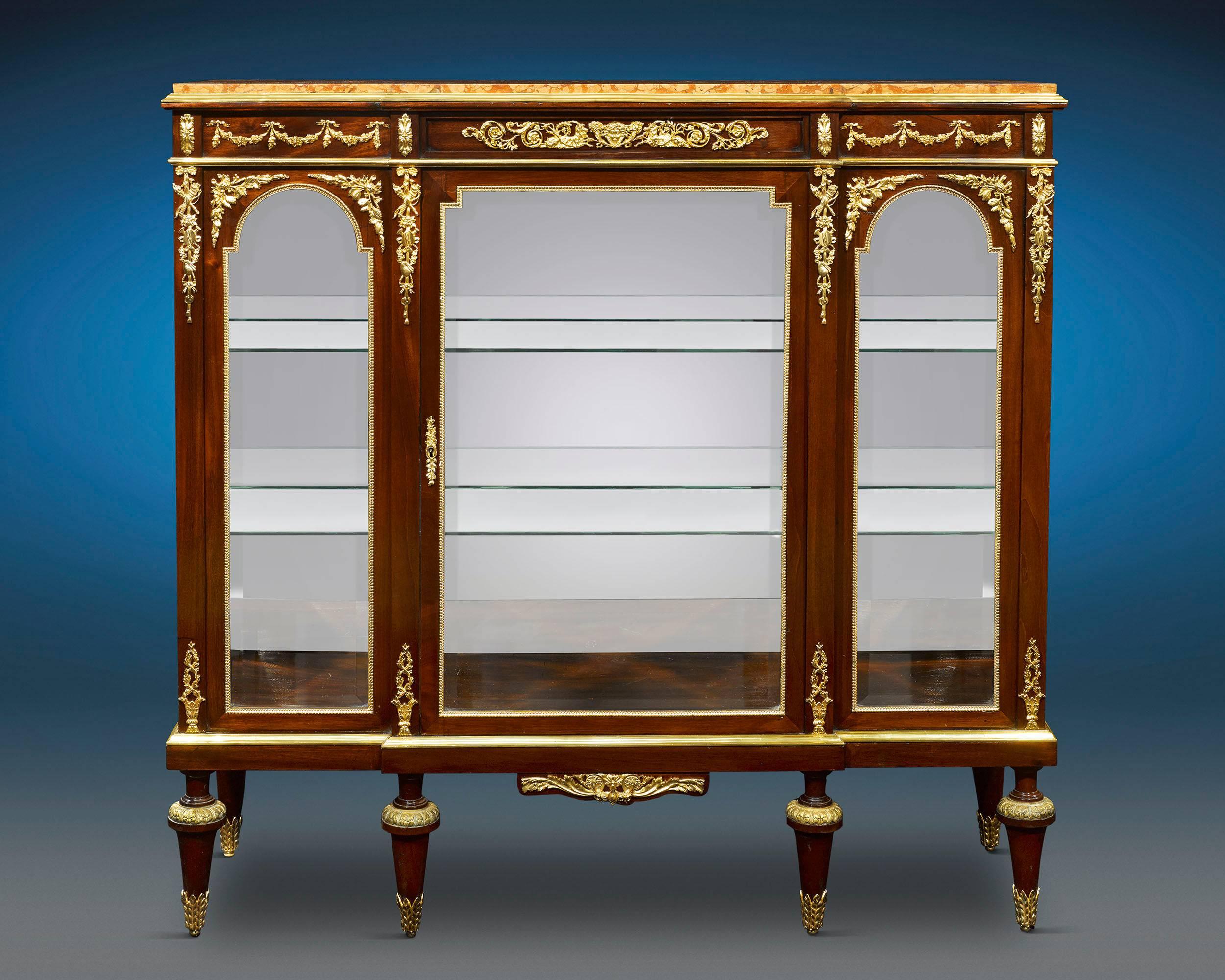 Fashioned in the Louis XVI style, this magnificent glass credenza has an opulent, yet classical feel. Crafted of luxurious mahogany, the extraordinary piece is bedecked with lavish ormolu mounts that beautifully accent the wood's rich hue. French