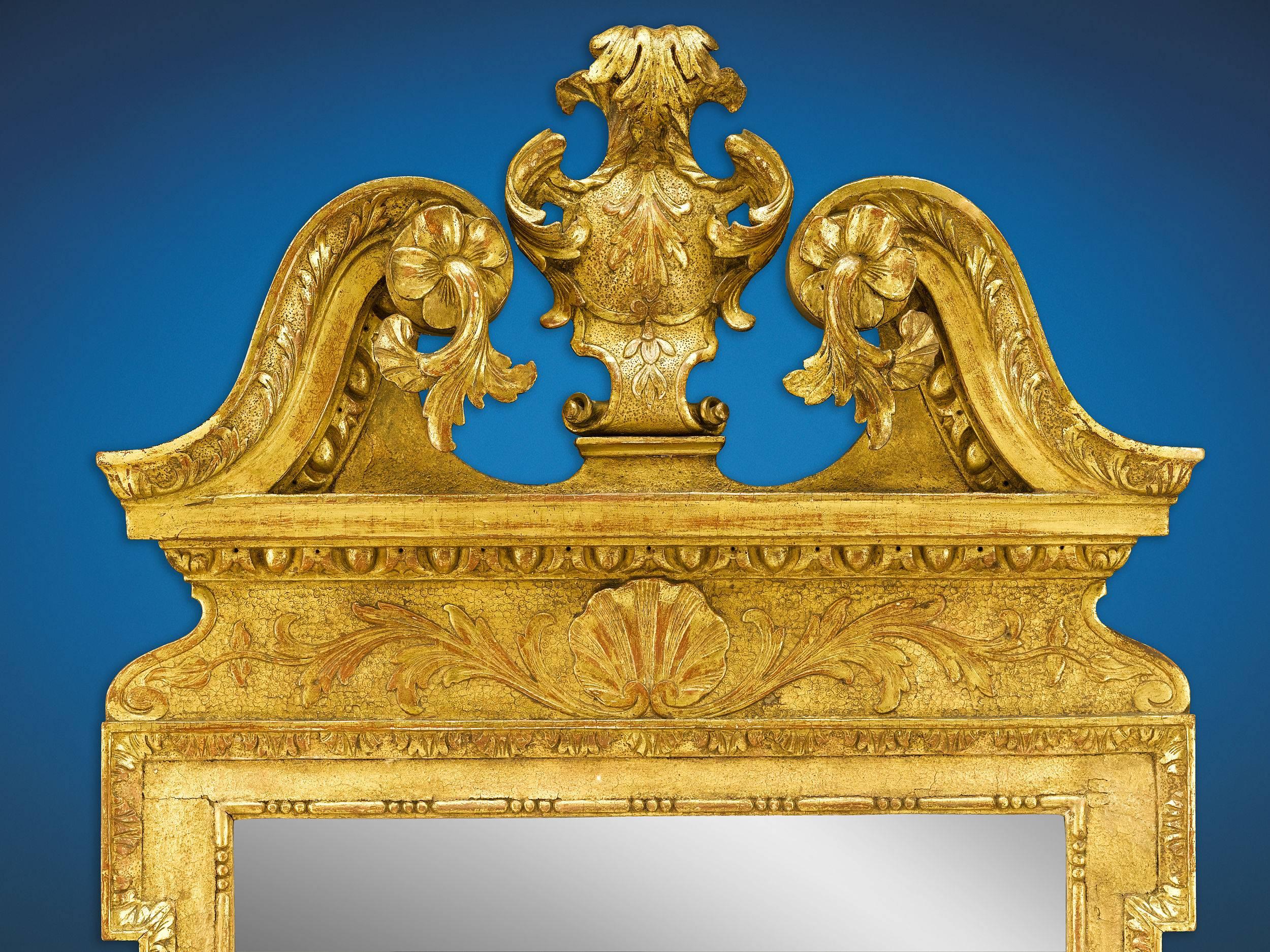 A rare and outstanding George II gesso gilt mirror, marked by a vast array of carved and applied decoration. Crowned with a spectacular broken pediment adorned with acanthus and flowers, the Palladian-style mirror showcases an elegant bead-and-reel
