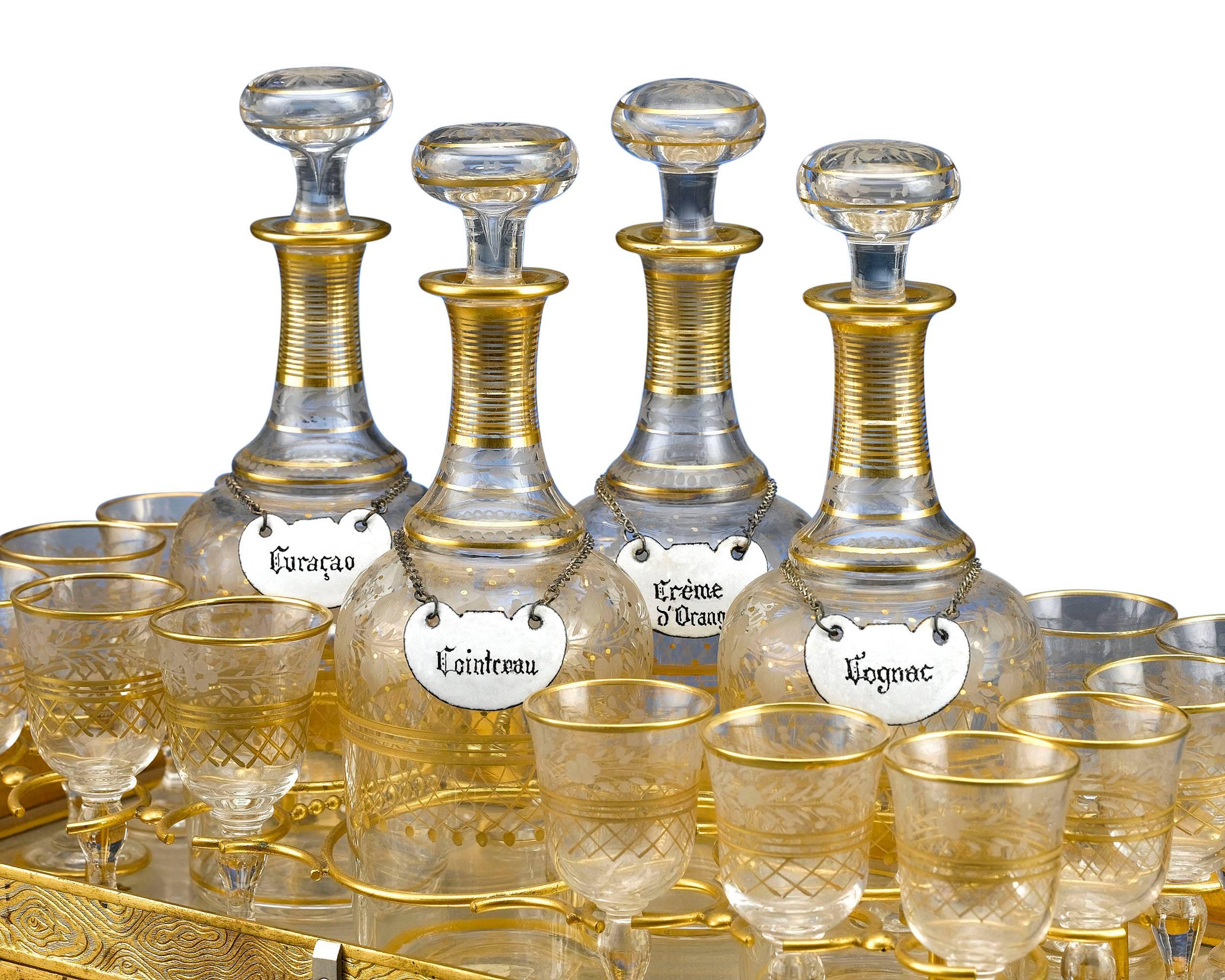 A wonderful and rare cave à liqueur, or Gentleman's Liqueur in the form of a gilt and engraved railway truck. The set is complete with four crystal decanters bearing colorfully enamelled labels (Cassis, Cognac, Anisette and Armanoal) and 16 cordials