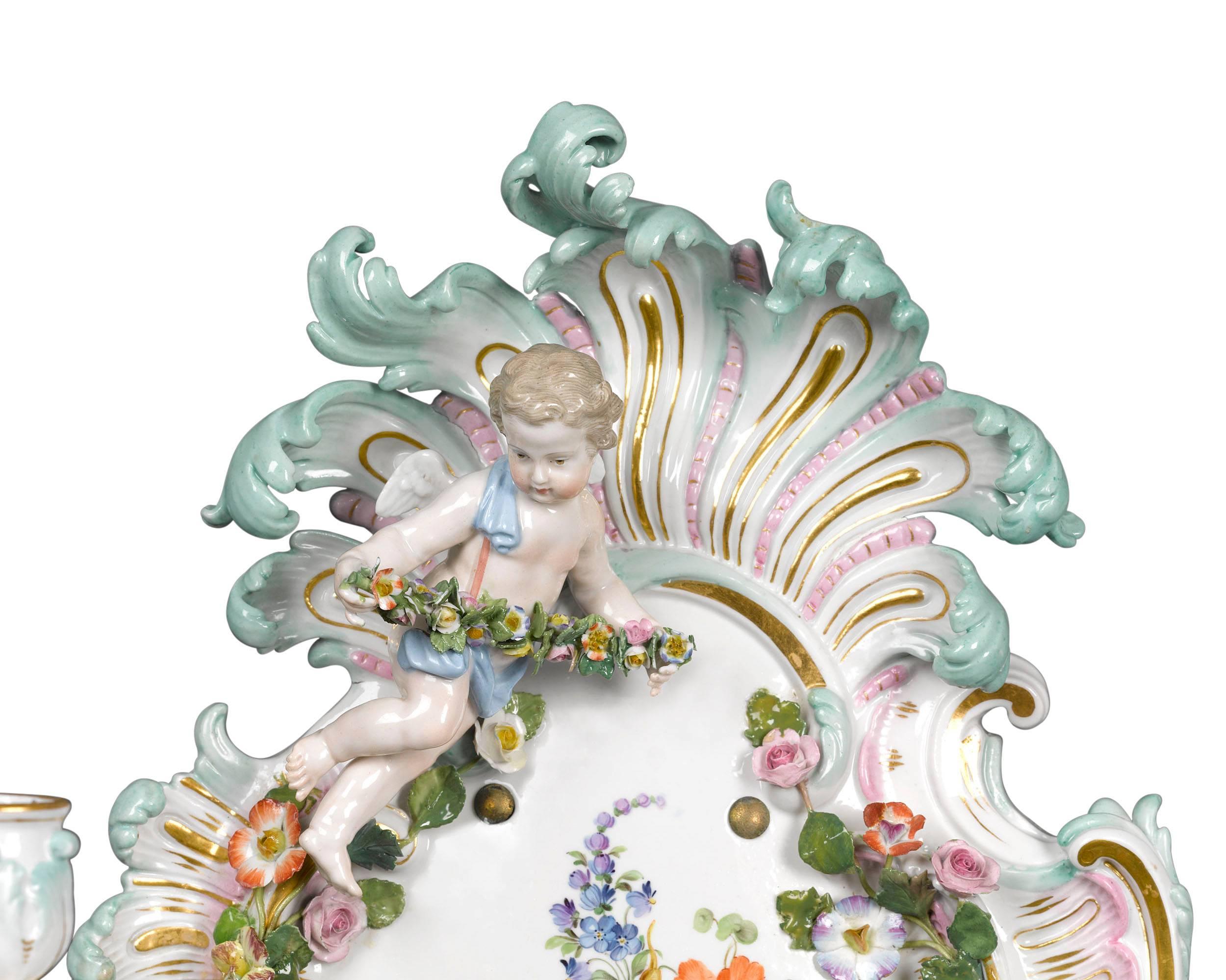 This enchanting pair of Meissen sconces exhibits the finest artistry for which this famed porcelain firm is known. Decorated with Meissen’s hallmark hand-painted intricacy, with delicate applied flowers and garland-bearing cherubs, the sconces are