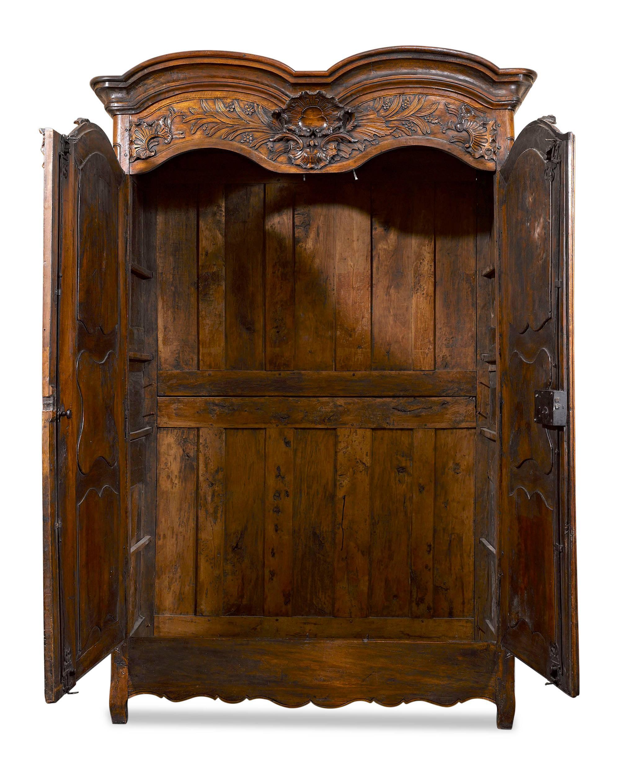 This majestic French walnut armoire is a stunning example of the Provincial style. Standing nearly nine feet high, this rare armoire featuring splendid rocaille carvings above its double doors and a wonderfully rich patina. Original mountings,