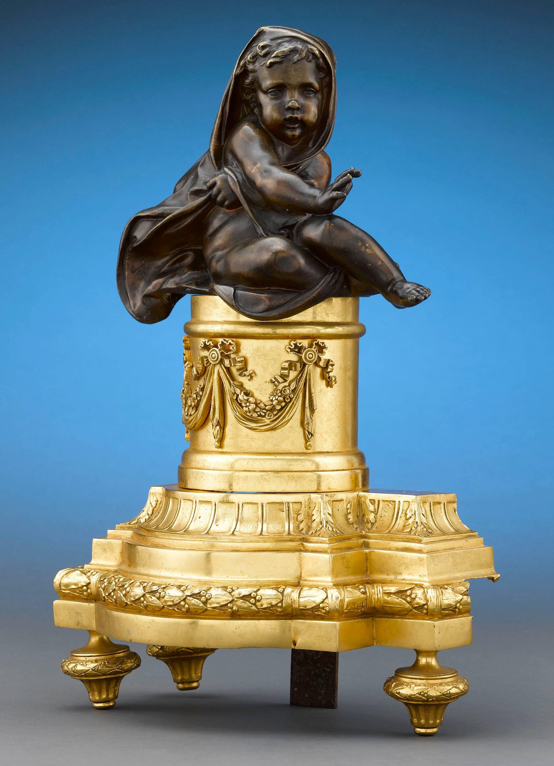 This wonderful pair of Louis XVI-style bronze chenets features patinated, cloaked cherub figures seated on ornate gilt bronze plateau and keeping themselves warm by the fire. Chenets, or andirons, were a staple in well-appointed homes, and were