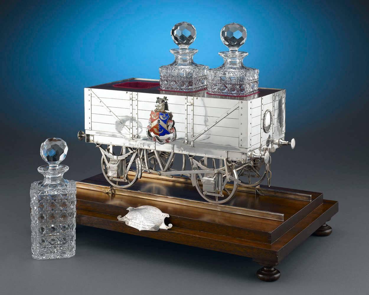 This rare and incredibly unique sterling silver decanter Stand is ingeniously designed in the form of a railway car. The Stand was presented to Municipal Alderman William Holdsworth, Chairman of the Water Commission, on July 13, 1904 at a ceremony