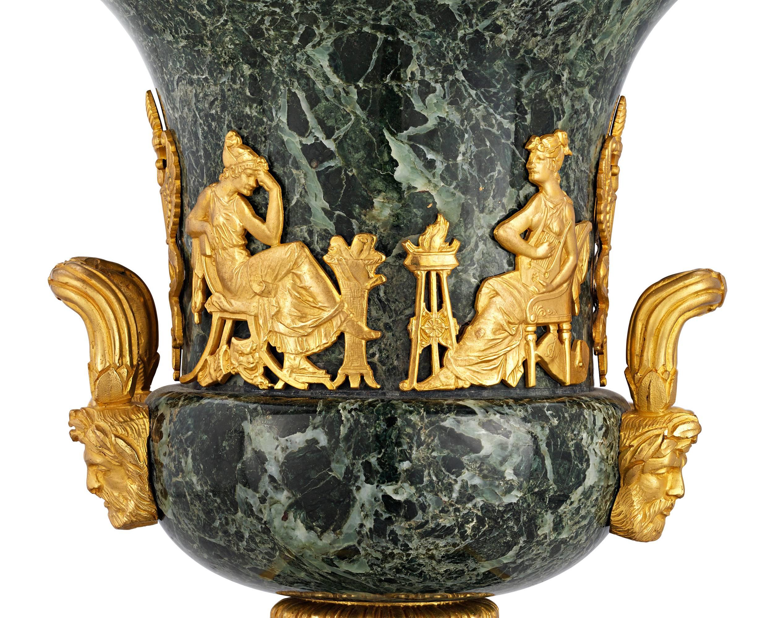 The classical grandeur of the Empire style is on display in this pair of verde antico marble and doré bronze urns. Crafted in an iconic krater form, the urns display a bold Greco-Roman influenced the design, including a stunning frieze motif