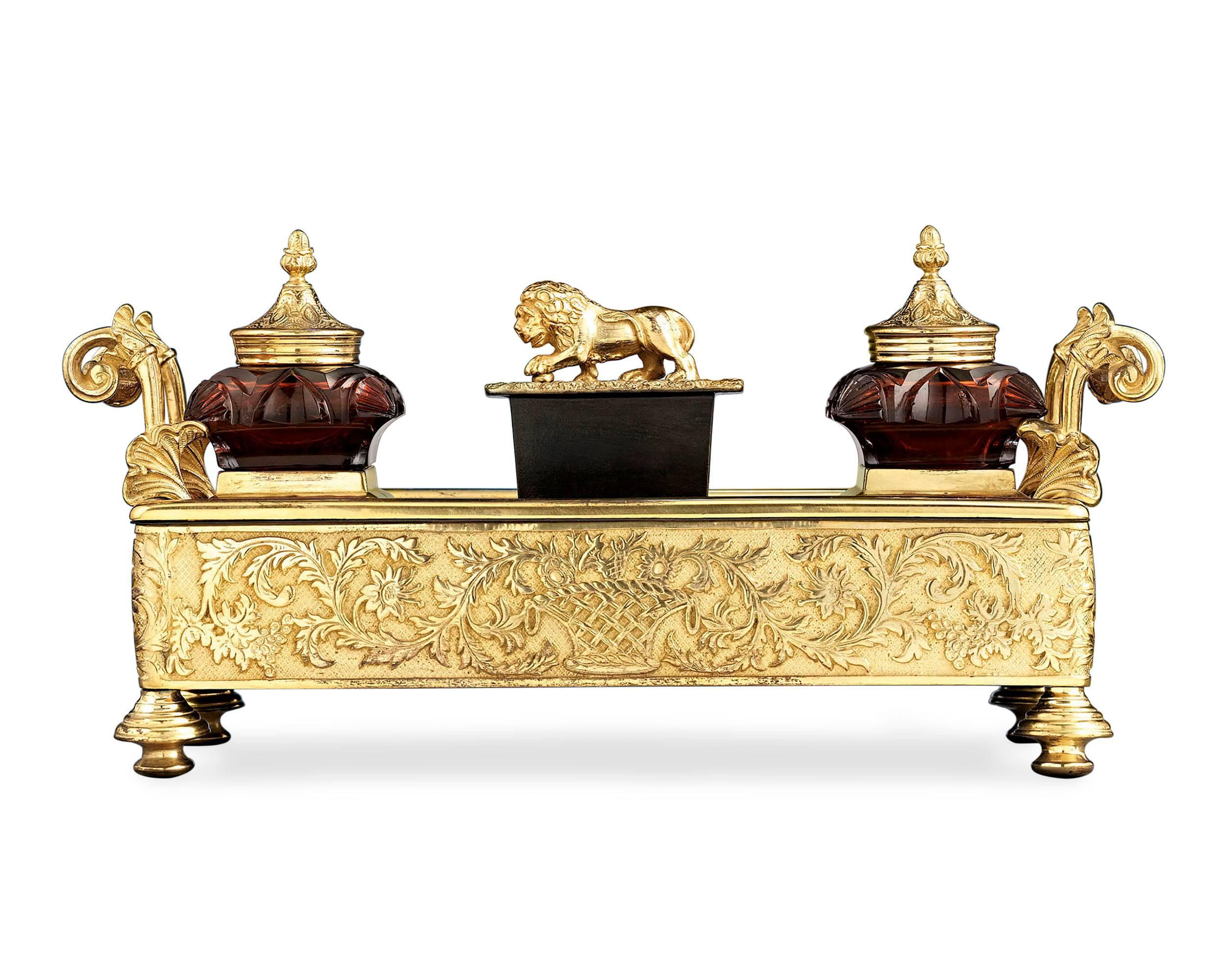 Fine bronze ormolu is beautifully contrasted by cranberry cut-glass in this Regency-period inkwell. This elegant desk accessory features a pair of removable glass inkwells, a wafer box surmounted by a gilt lion finial and a pen tray adorned with a