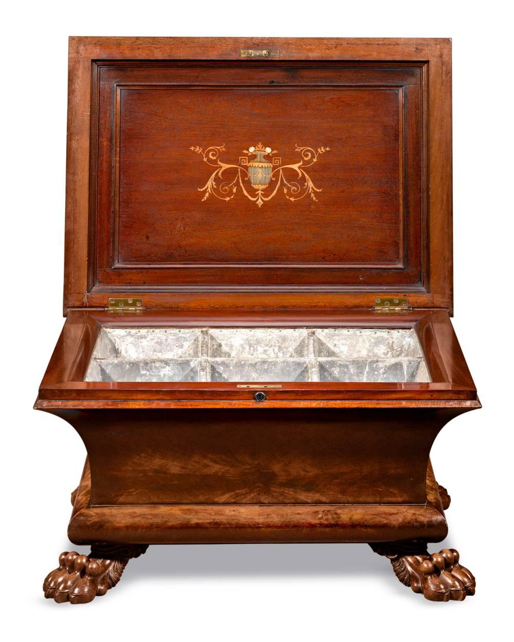 This refined William IV period wine cellarette is crafted of rich mahogany and boasts beautifully carved details. The sarcophagus form is distinguished by handsome lion paw feet and intricate inlay accents under the lid. Complete with its grape