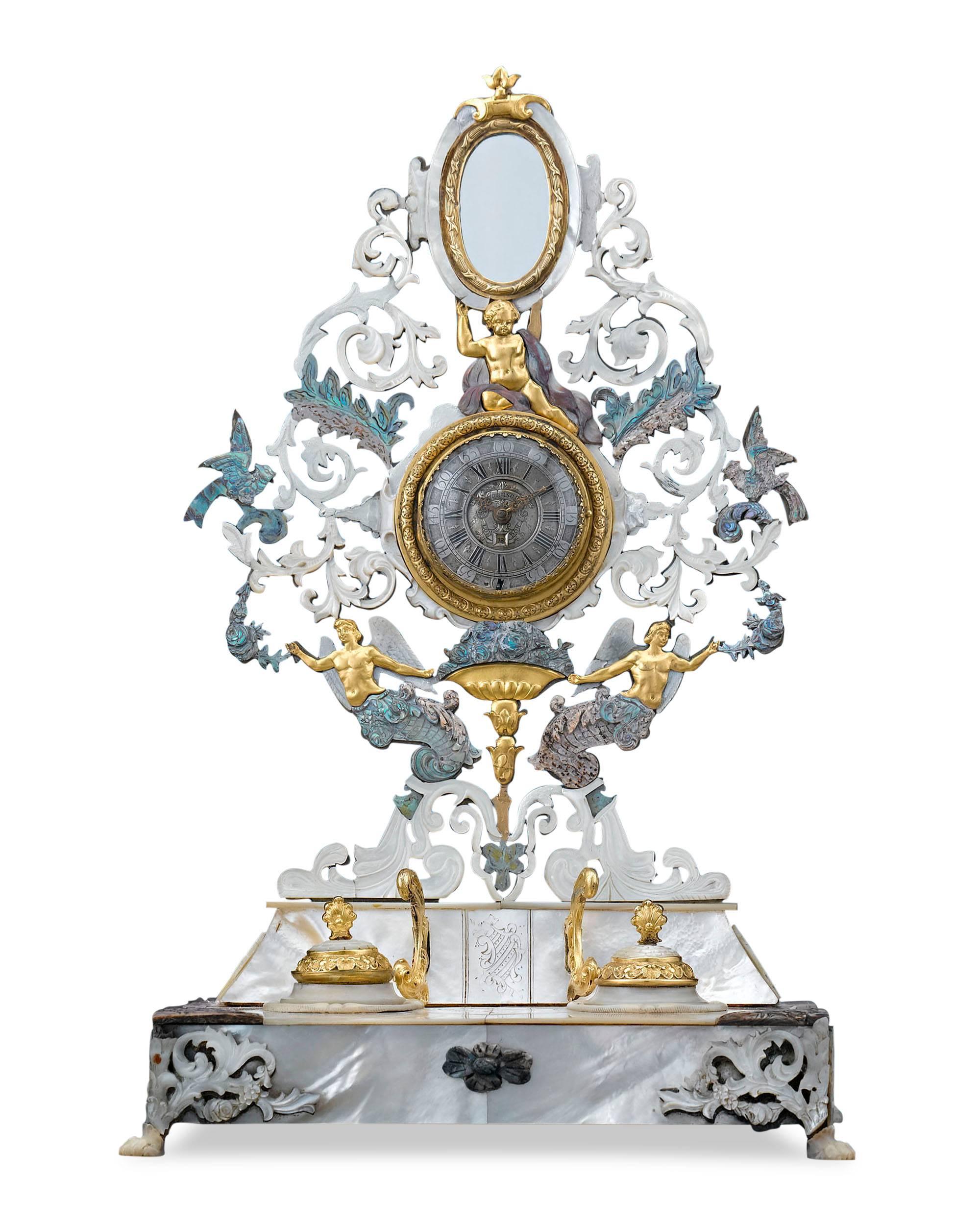 Shimmering mother-of-pearl envelopes this outstanding watch holder and inkwell. The magnificently detailed, pierced screen secures a timepiece and diminutive mirror, while the base holds the removable inkpots and watch-holder mountings. Doré bronze