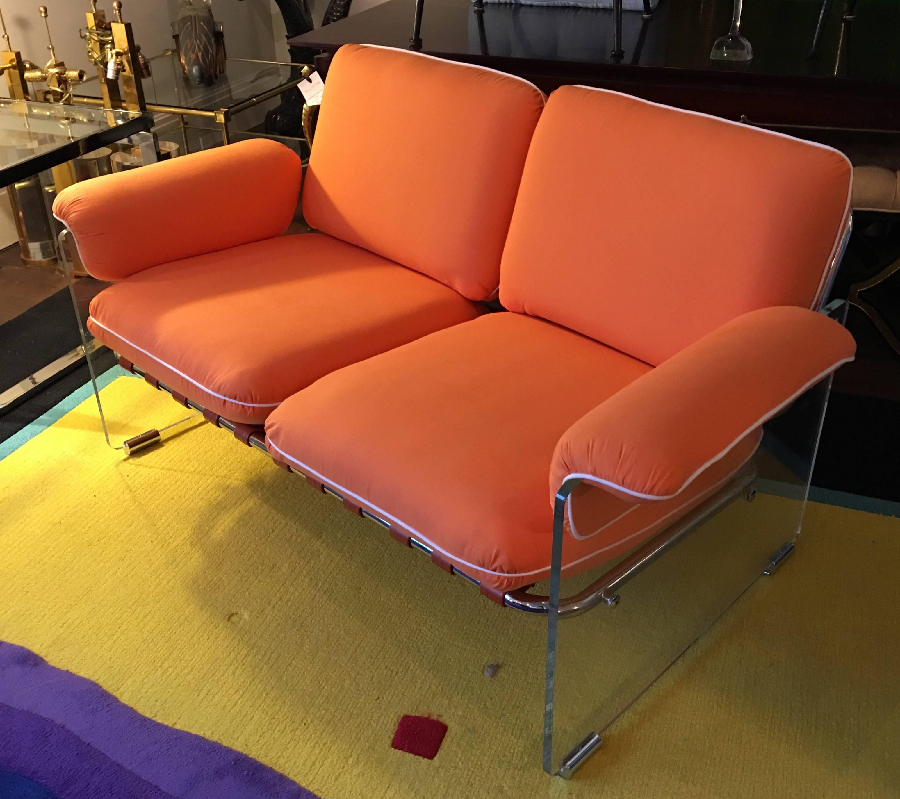 This Pace Lucite and chrome loveseat features tubular chrome back and seat structure flanked by Lucite panels which gives the piece the appearance of floating. Newly upholstered in a stunning orange fabric with white piping, circa 1970.