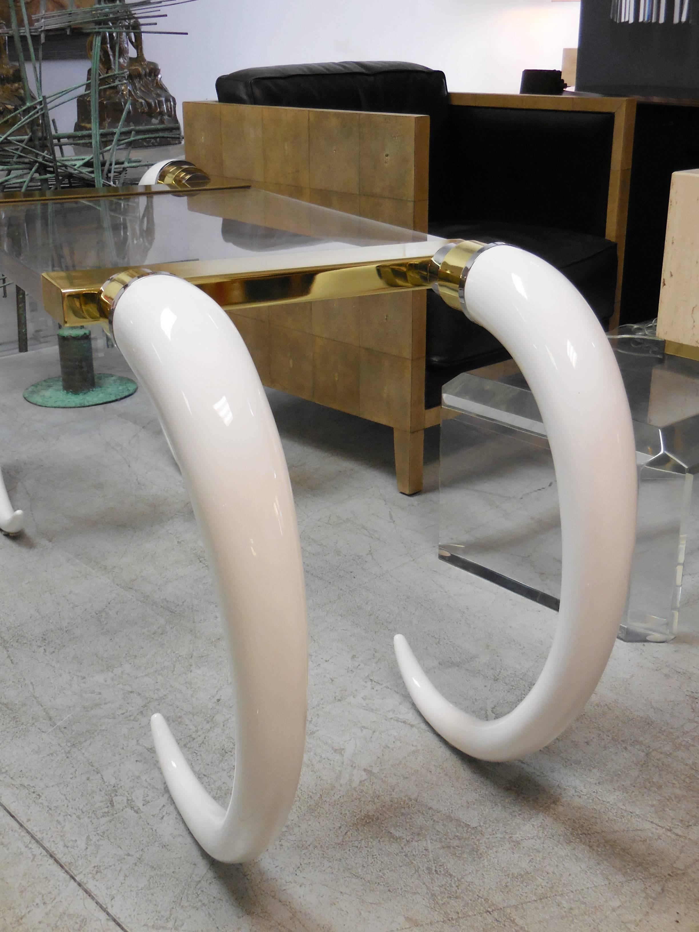 A wonderful brass and faux elephant tusks desk. With thick Lucite tabletop makes the tusks appear to float to either side, circa 1970s.