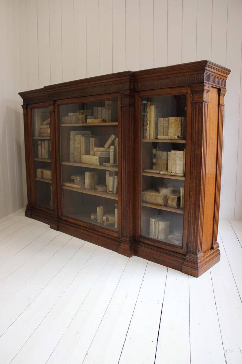 A good quality and imposing late 19th century oak architectural breakfront bookcase by Howard & Sons (applied manufacturer's ivorine label), the fluted cornice above the three glazed doors enclosing adjustable shelves.