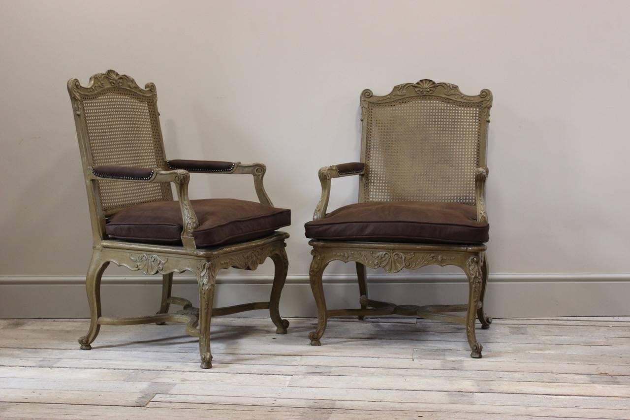 A good pair of Louis XV style painted and caned open armchairs, the cushions and arm-rests recently recovered in leather, French, early 20th century.
 