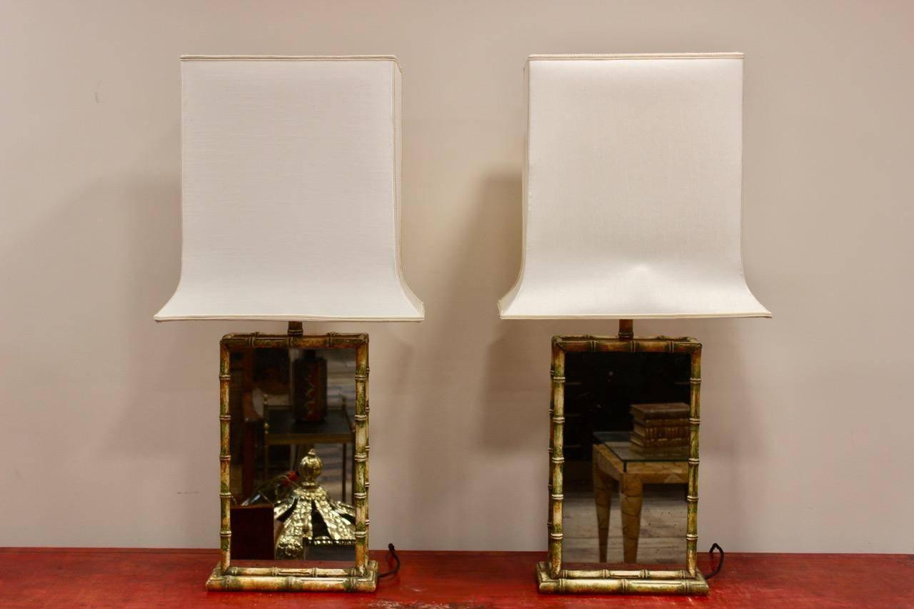 A stylish and unusual pair of circa 1970s faux bamboo and mirrored-glass table lamps with their original distinctively shaped shades.
    