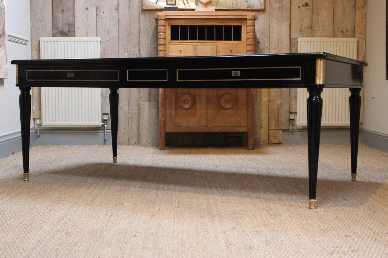 A very smart and unusually large, circa 1920s French ebonized double-sided partner's desk in the Louis XVI taste, retaining the original brass and leather top, with two deep drawers on each side. This elegant desk will make a statement in any room.