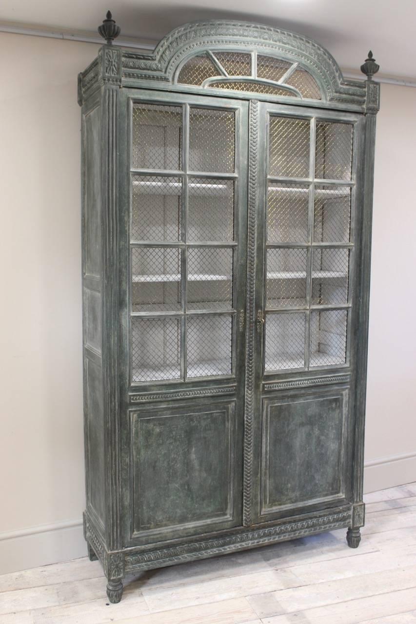 A wonderful and richly-carved circa 1910 French Louis XVI revival bookcase with brass grille doors enclosing four adjustable shelves (later painted finish)