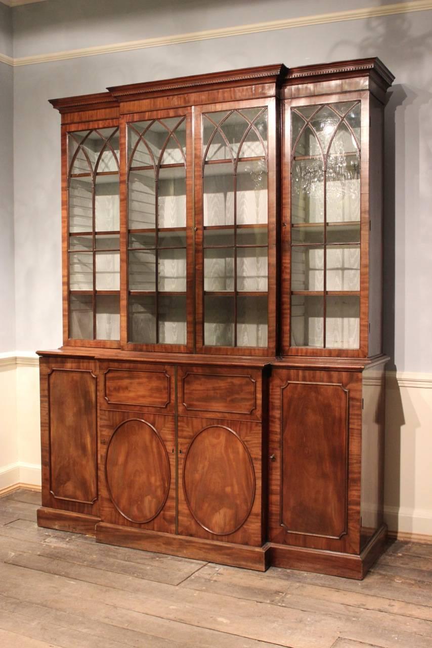 A fine quality and with elegant proportions, George III English mahogany breakfront bookcase with dental moulded cornice and gothic arched glazed doors with outline moulded panel doors on a plinth base. The interior covered in silk , with adjustable