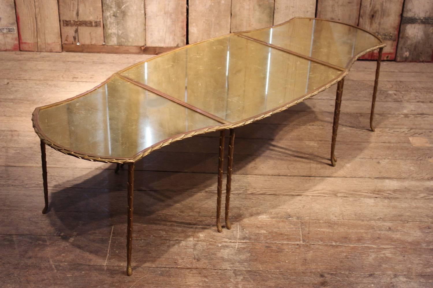 A glamorous and fine quality cast and gilt bronze coffee table, attributed to Maison Baguès, composed of three sections, with a verre églomisé top, the frame cast as running palm leaves, French, 1950s.