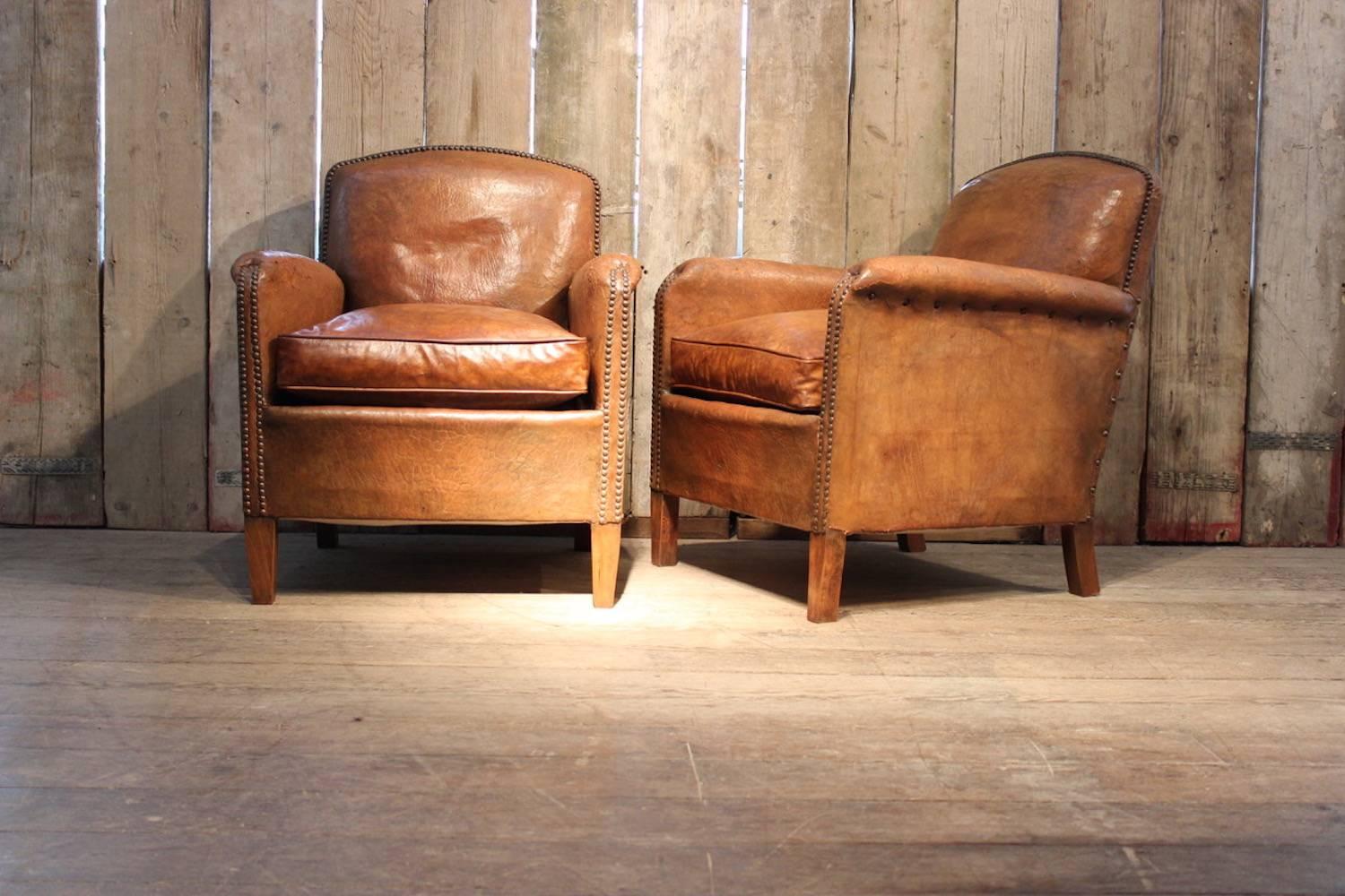 A good pair of early 20th century French leather club armchairs with original tan leather and close-nailing, the seat cushions re-covered, with square tapering legs.