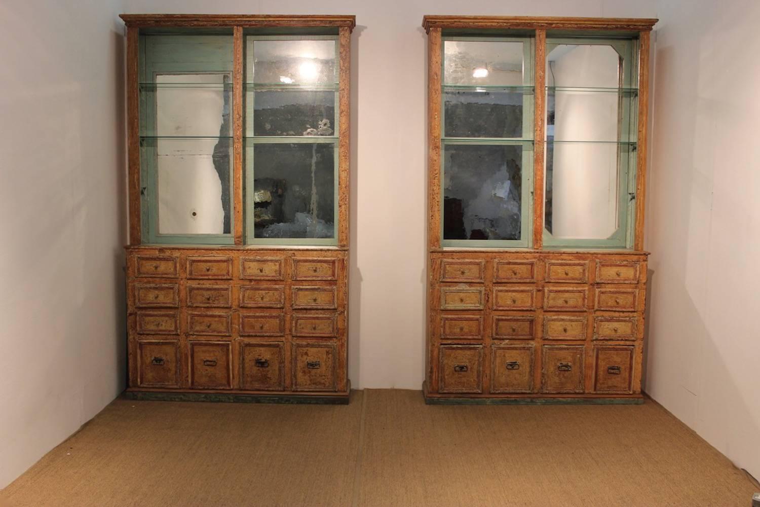 An unusual and large pair of Spanish display cabinets retaining their original paint, with mercury glass lined interiors, each with six shelves above an arrangements of 16 drawers, originally from a patisserie, 19th century, with some later