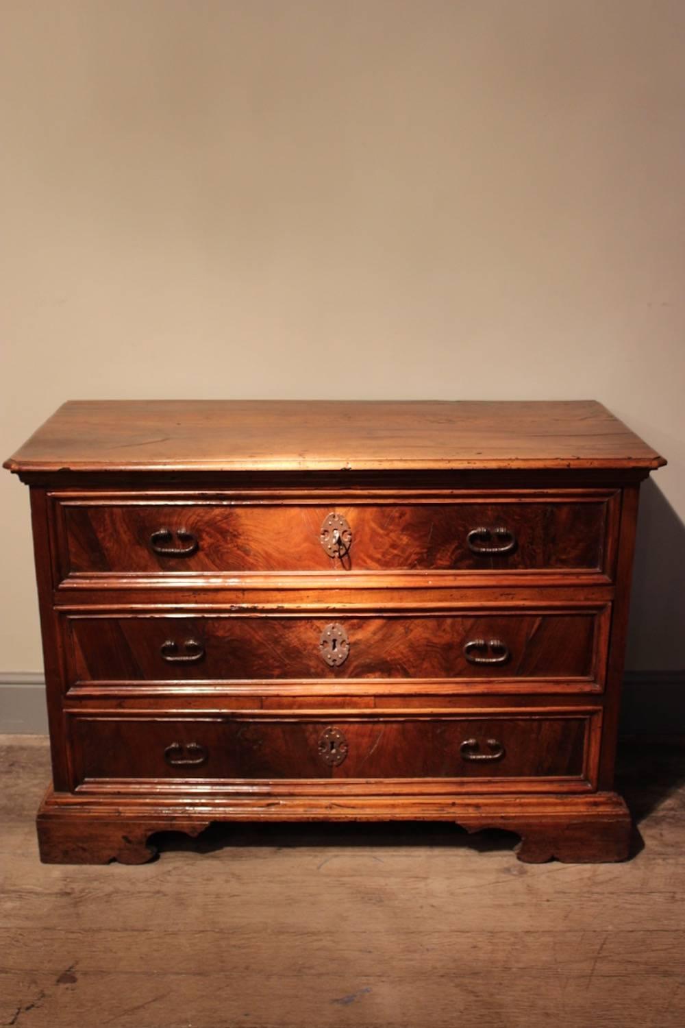 A substantial mid-18th century solid walnut and figured walnut veneered three drawer commode with the original iron handles, escutcheons and over-scaled bracket feet, probably Tuscan, circa 1750.