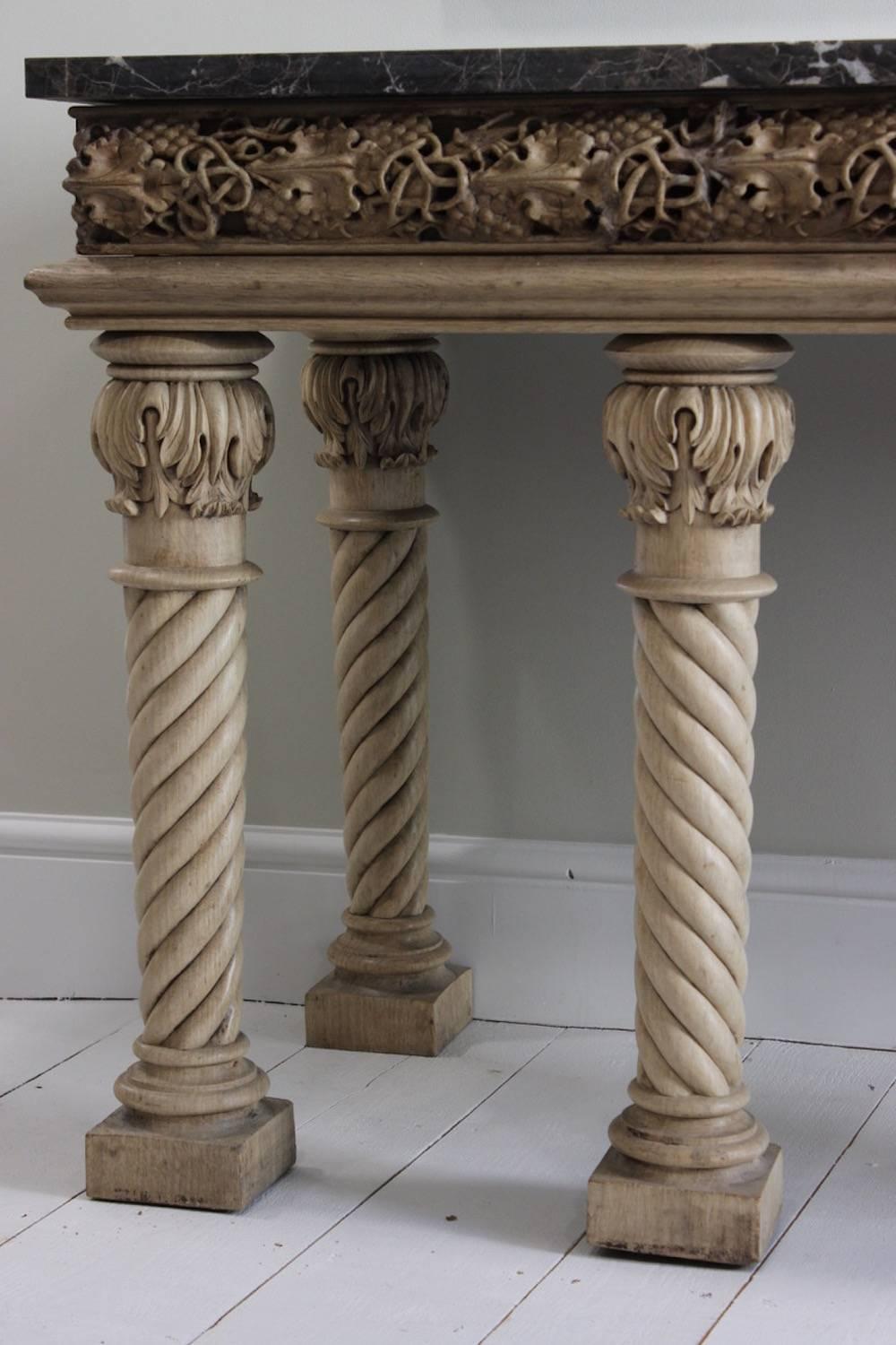 A large and imposing bleached oak country house console table with a later marble top above a frieze carved in deep relief with leaves and berries, on six spiral turned and acanthus-carved tapering legs with block feet, English, late 19th century.