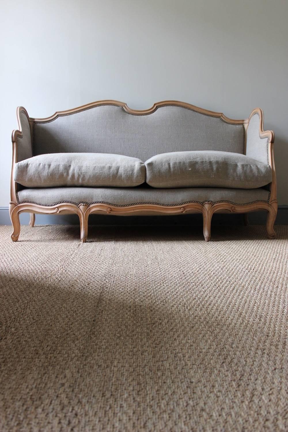 A good quality beechwood sofa or canapé in the Louis XV style, with close-nailed padded back and arms, all newly recovered in a neutral linen fabric and supplied with two new feather cushions, French, circa 1900.