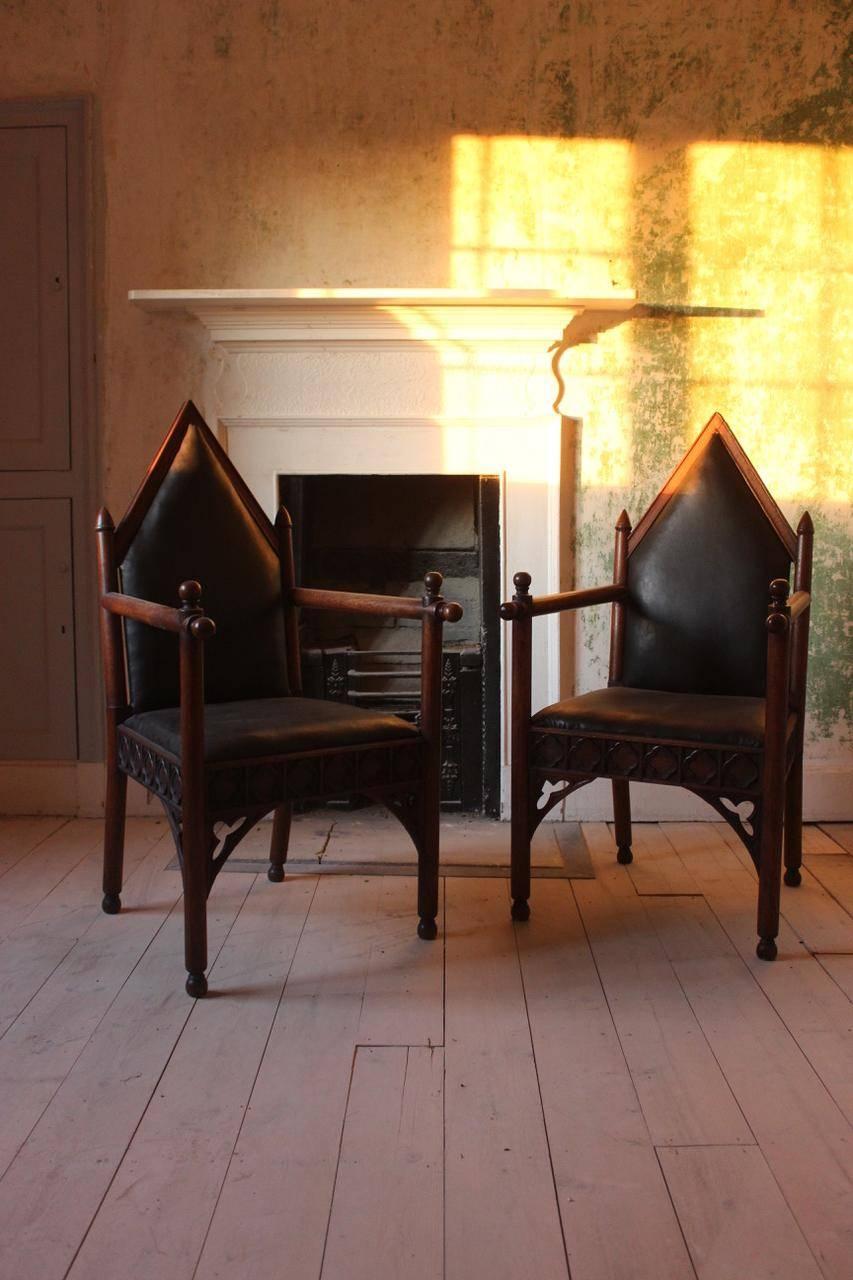 A very smart and visually arresting pair of oak armchairs in the Gothic style with contrasting black leather upholstery, English, 19th century.