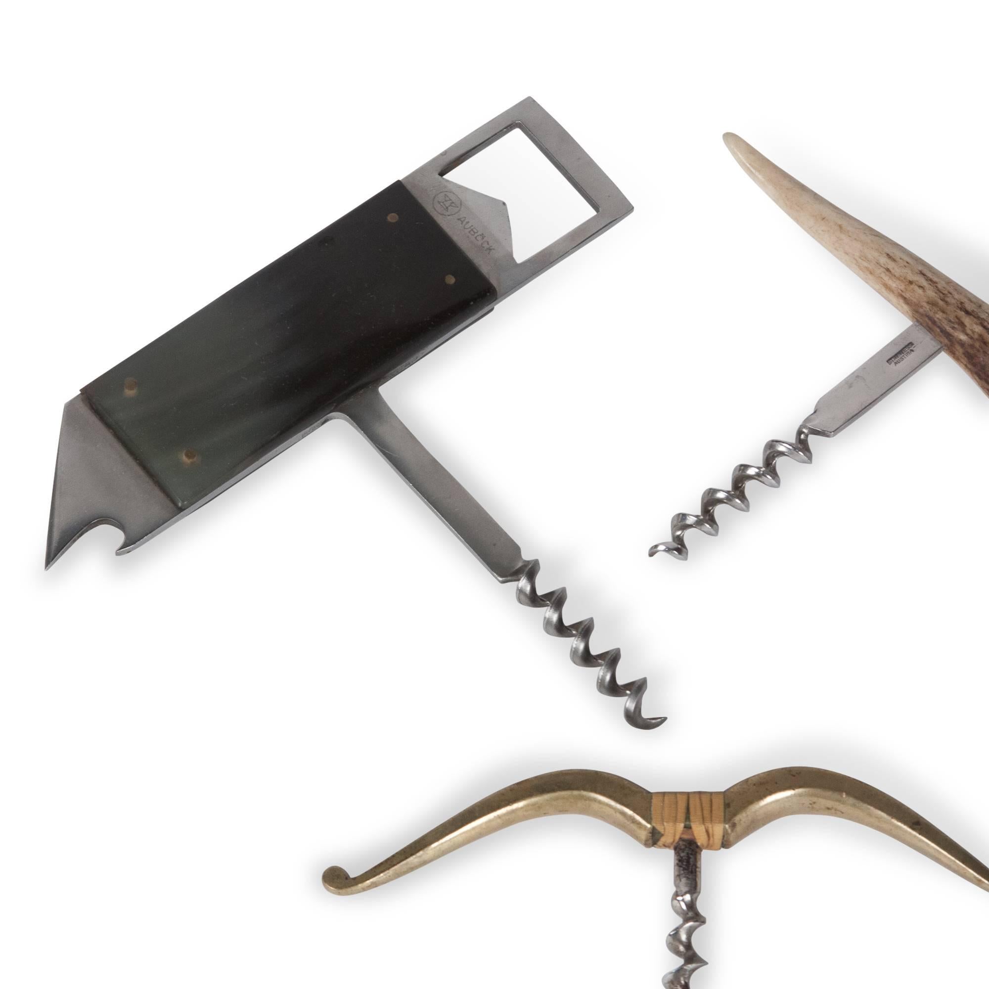 Three corkscrews.
Top left: Horn clad stainless steel bottle opener and corkscrew, by Carl Aubock, Austria, 1950s. Etched signature. Width 5 1/2 in, height of handle 1 5/8 in, length 5 1/4 in.  
Top right: Horn or tusk corkscrew, stainless screw