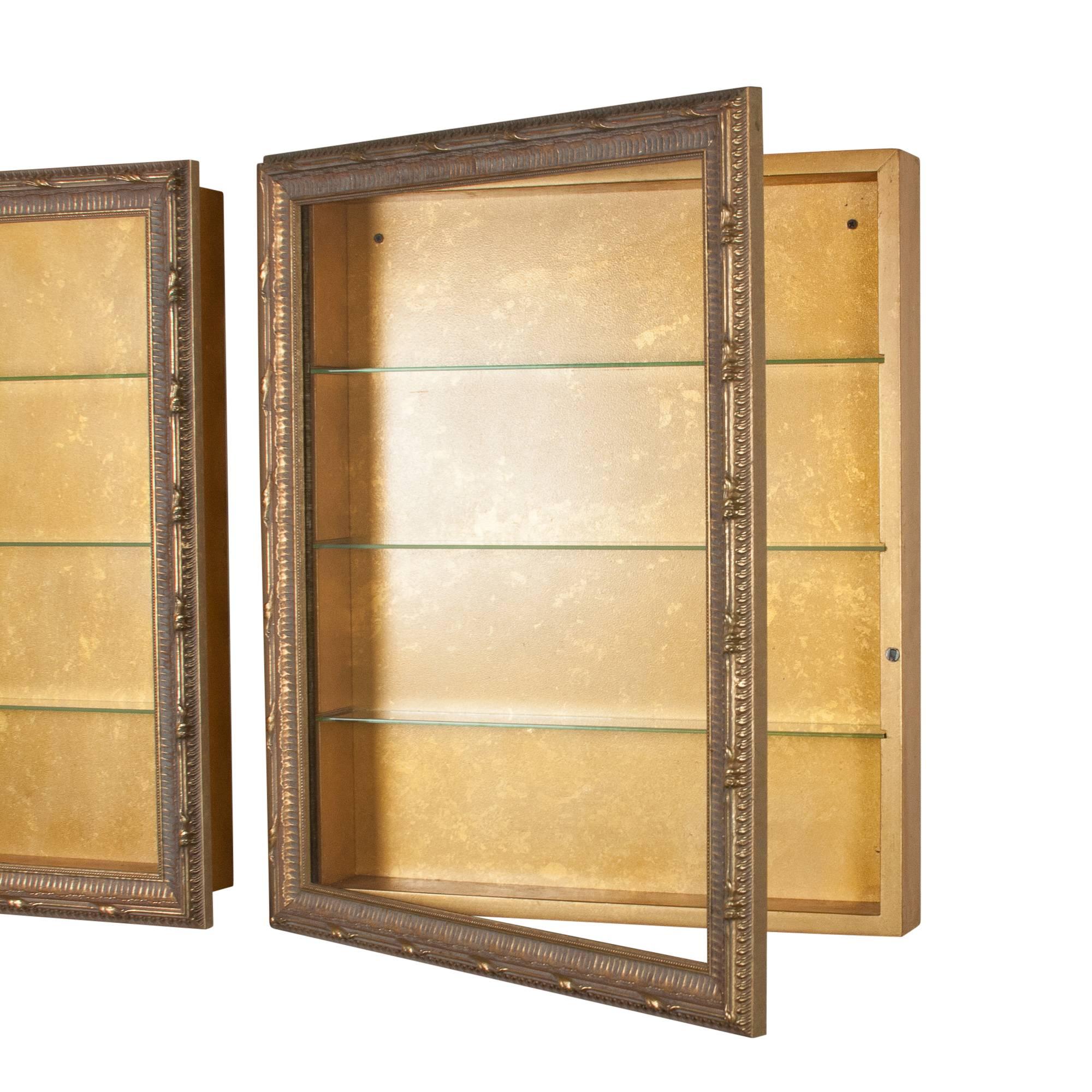 Pair of wall-mounted vitrines, carved giltwood frames, glass front hinged doors, each with four interior shelves, mottled gilt painted interior, American, 1950s. Measures: Height 27 1/4 in, width 23 1/4 in, depth 4 1/4 in. (Item #2385 sats)
