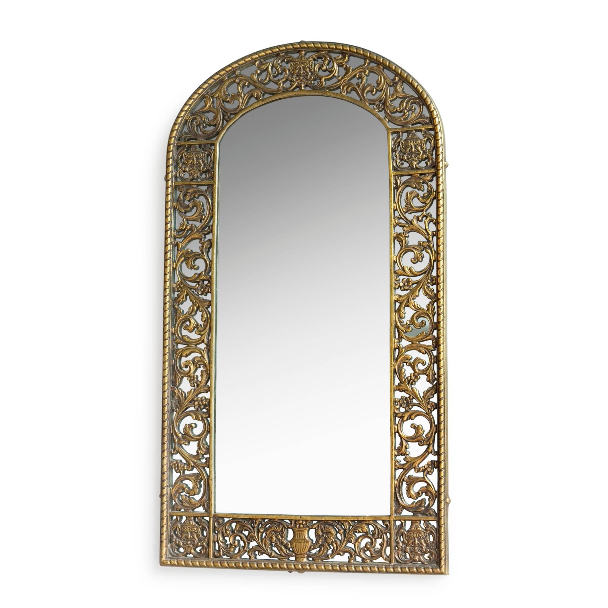 Cast bronze arched top foliate and figural form frame mirror, detailing masks, urns and scrolling leafage, by Oscar Bach, American, 1920s. Measures: Height 34 1/4 in, width 18 3/4 in. (sats)
 