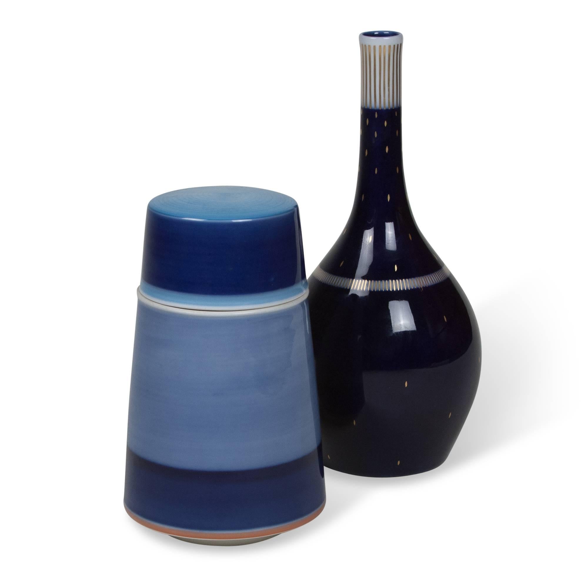 Two porcelain pieces:
On left: Cobalt blue and blue porcelain lidded circular container, with banding, by KPM, German 1950s. Signed. Measures: Height 5 3/4 in, diameter 3 1/2 in.
On right: Cobalt blue glazed porcelain bottle, with gold decoration