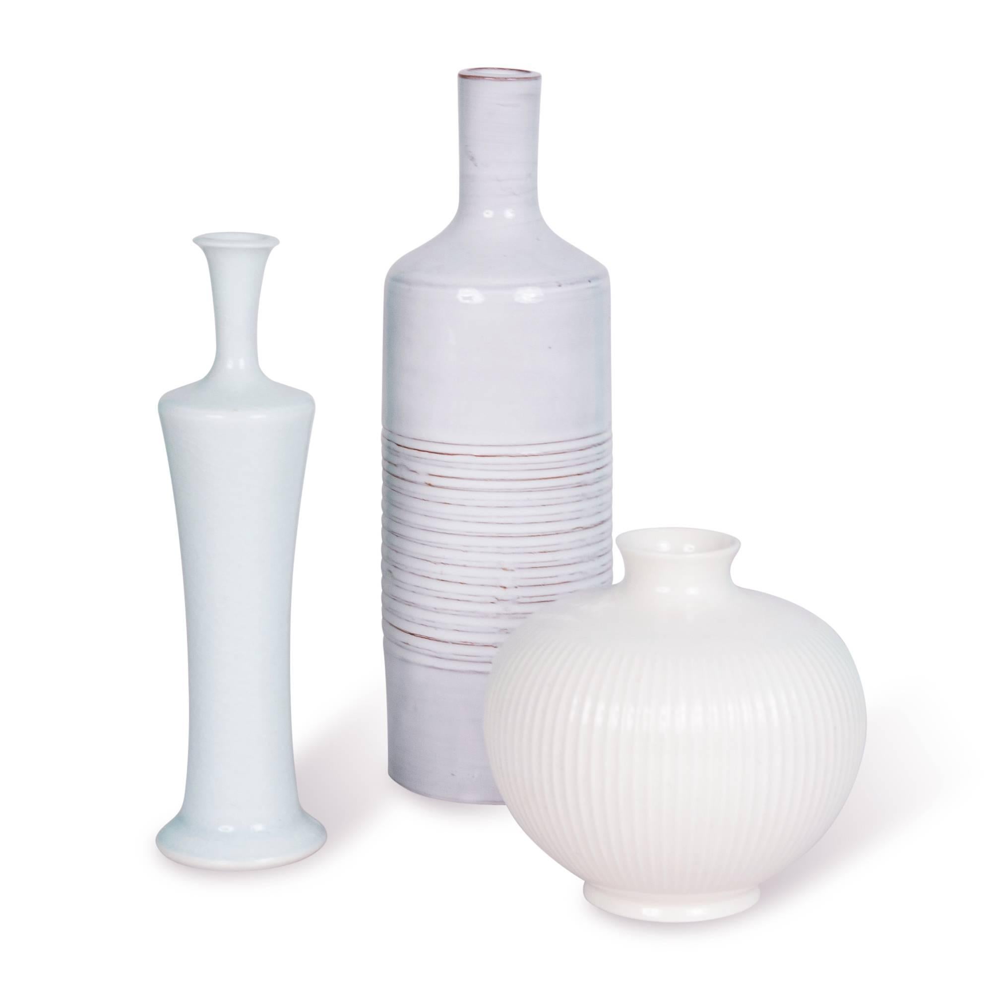 Set of three:
On left: Porcelain bulbous form vase, with grooved sides and flared rim by Royal Copenhagen, Denmark, 1960s. Measures: Height 4 in, diameter 4 1/2 in.

Center: Grey-white bottle form ceramic vase, with long neck, and grooved bands