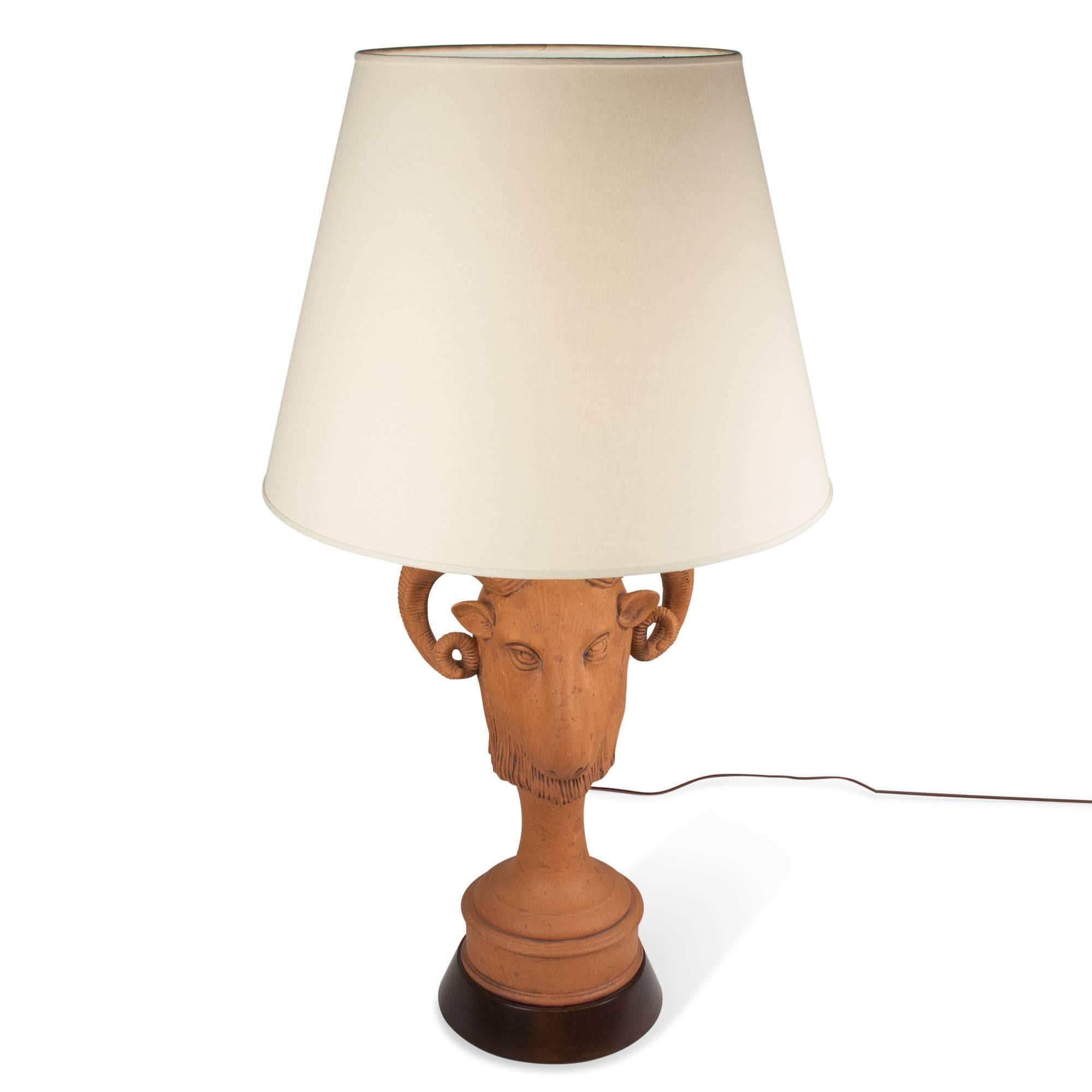 Terra cotta horned ram's head table lamp on wooden base by James Mont, American, 1950s. Stamped signature. In custom linen shade. Measures: Overall height 35 in, largest diameter of base 9 in. Shade measure height 15 in, top diameter 12 in, bottom