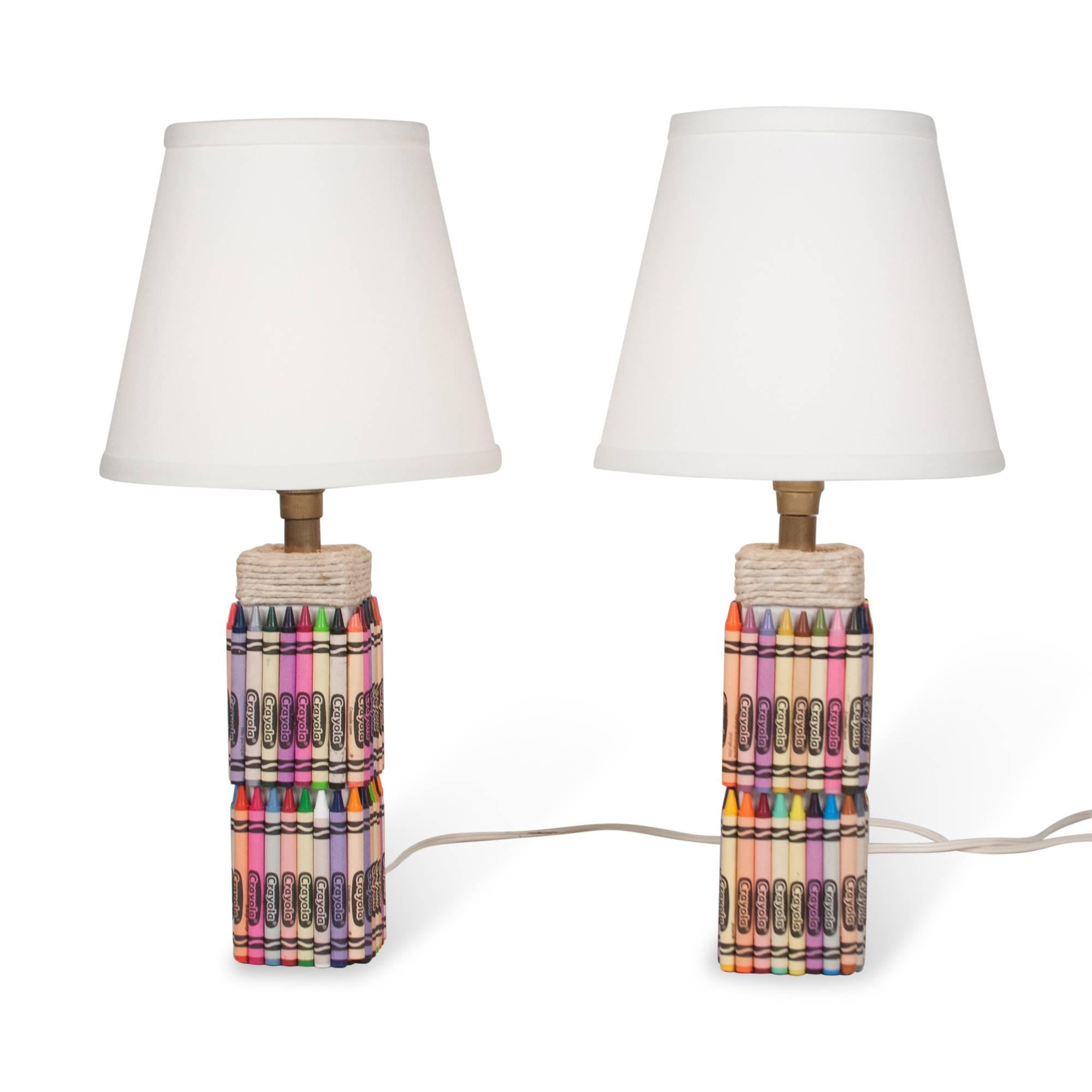 Pair of crayon table lamps, square ceramic form with Crayola brand crayons of assorted colors applied to surface, with wrapped rope at top of base, in custom linen shade, American, 2000s. Measures: Overall height 16 1/2 in, base is 3 in square.