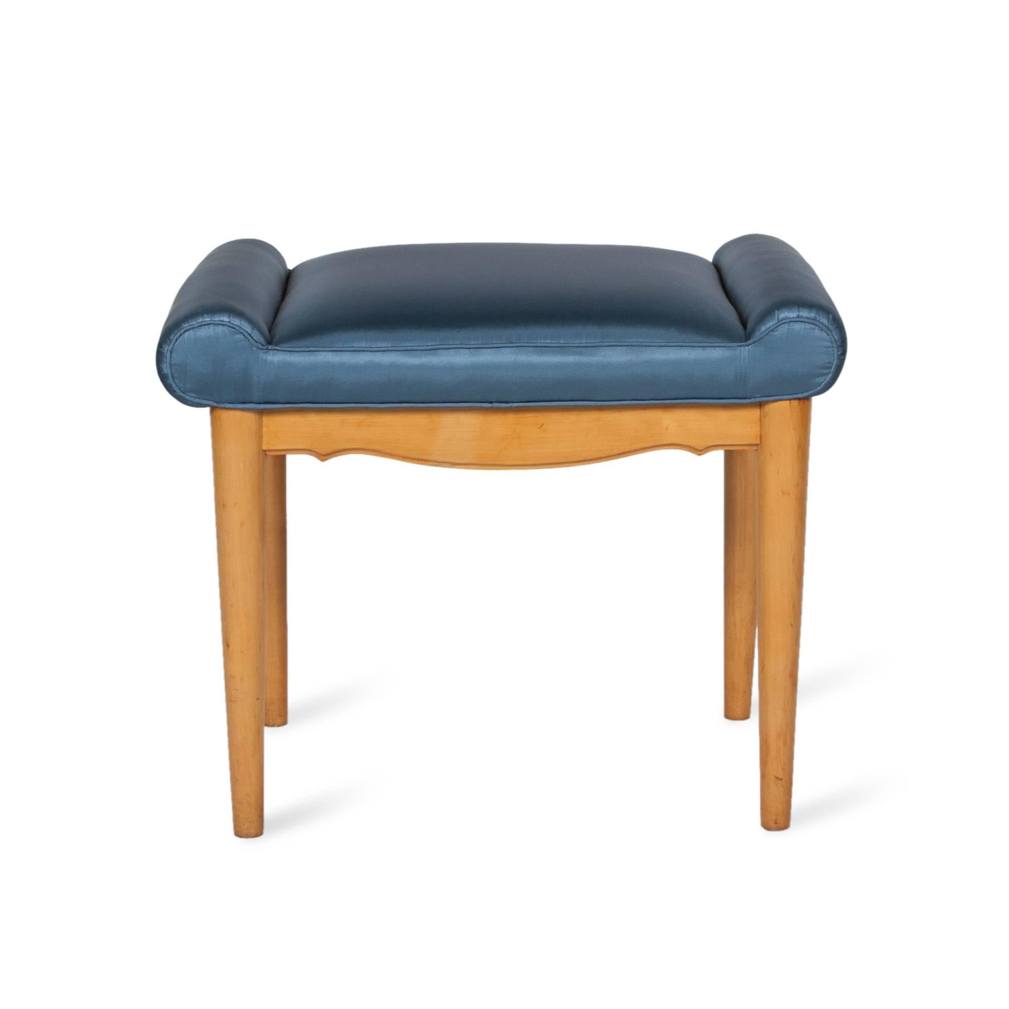 Sycamore vanity bench with scroll seat and apron, light blue satin upholstery, round tapered legs, American, 1930s. Measures: Width 23 in, depth 16 in, height 18 in.