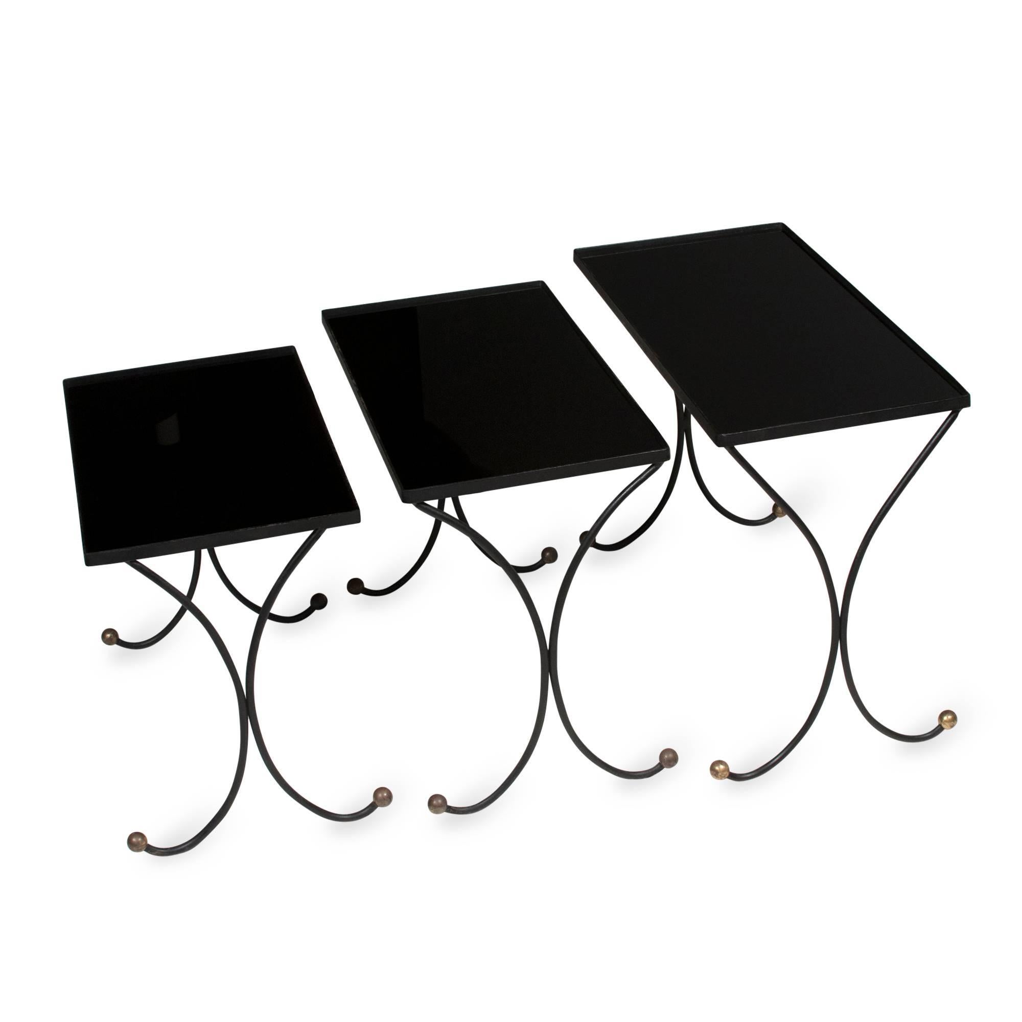 Set of three iron and black glass top nesting tables, curved legs with brass ball feet, French, 1950s, in the style of Jean Royère. The largest measures 24 x 12 in, height 18 3/4 in. (Item #2056). (sats)
