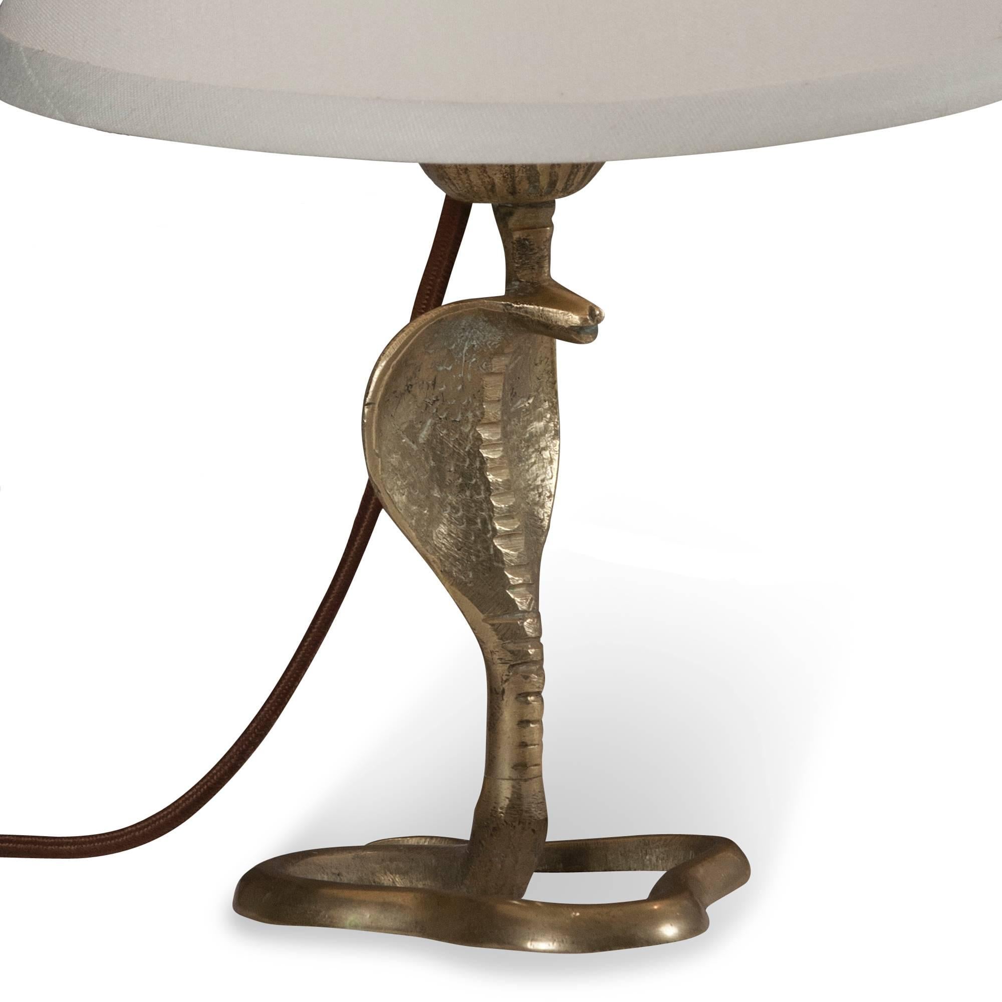 Pair of bronze cobra form table lamps, the serpent standing with hood open and body loosely coiled, French, 1930s. In custom silk shades. Overall height 14 in, base measures 4 in x 4 1/4 in, shade measures top diameter 5 1/2 in, bottom diameter 8