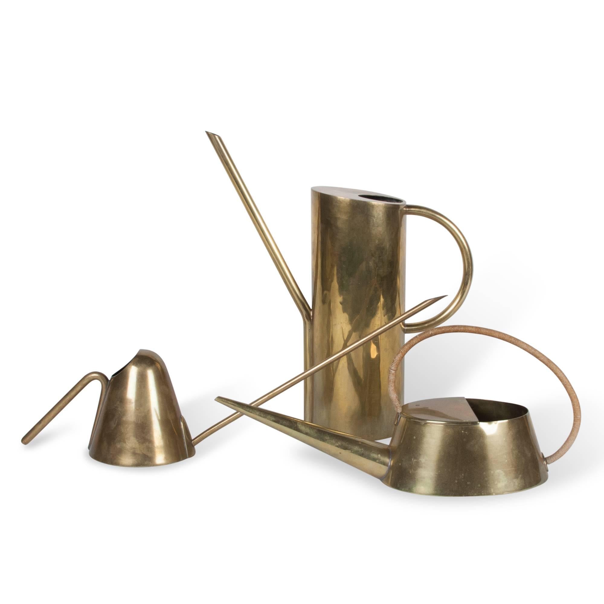 Three brass watering cans, from left to right.
1) Brass watering can, rounded cone shaped body with long spout, by Carl Auböck, Austria, 1950s. Length from spout to handle 18 1/2 in, diameter at bottom 3 3/4 in, height to top of spout 6 3/4