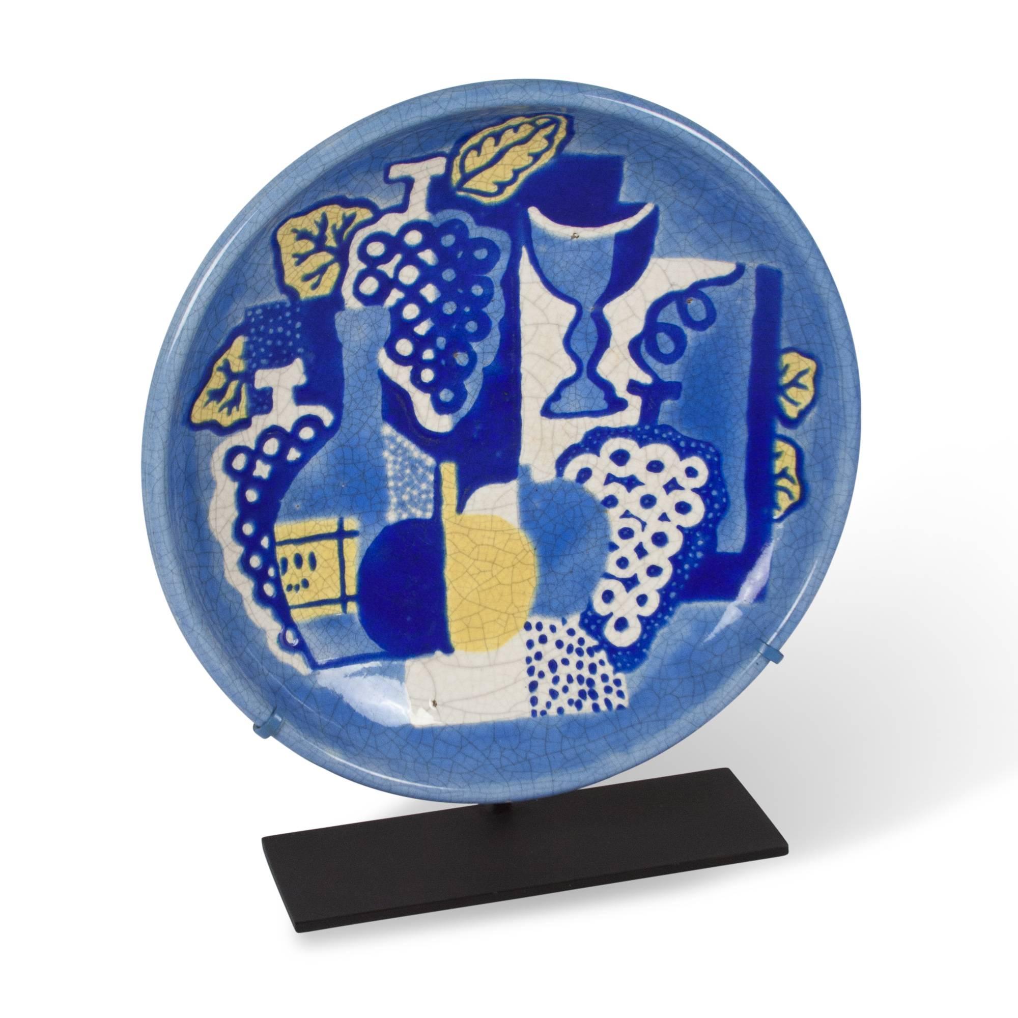 Ceramic charger, decorated with an abstracted cubist style still life against a blue ground, Atelier Primavera and Longwy, French 1930s. On a custom steel stand. Signed to back. Measures; Overall mounted height 17 in, diameter of ceramic 15 in, base