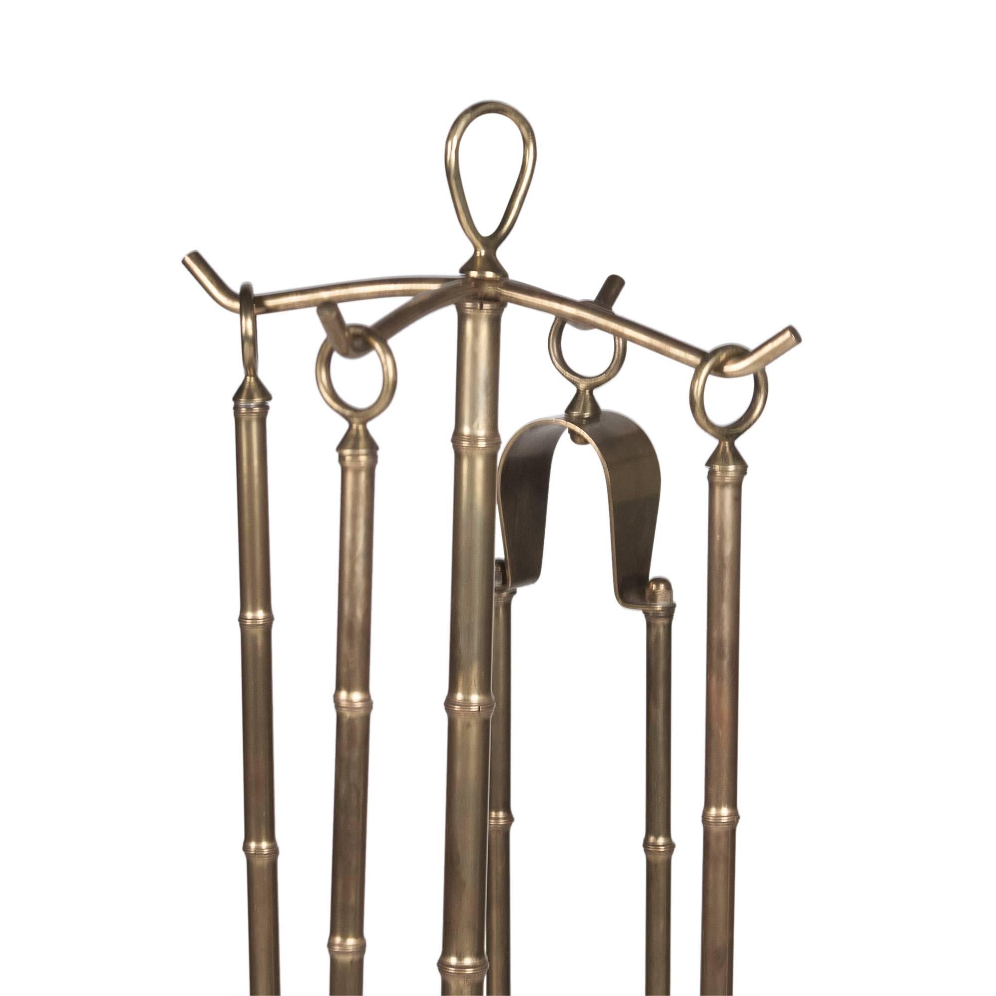 Four-piece fireplace tool set, in bronze and iron, faux bamboo with ball feet, comprising a shovel, broom, log tongs and poker on a stand, by Jacques Adnet, French, circa 1950. Overall dimensions: 27 in. H x 10 in. W x 10 in. D.