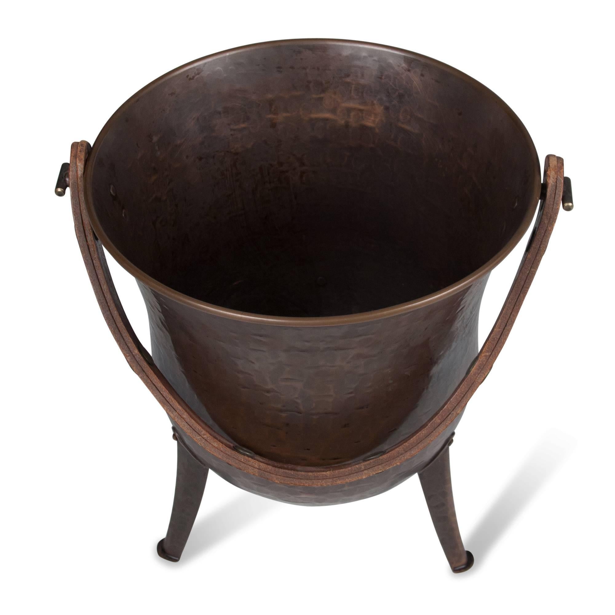 Textured and patinated copper metal bucket, raised on three legs, with leather strap handle, Germany, 1930s. Measures: Height 10 1/2 in, depth 9 1/2 in. (sats)