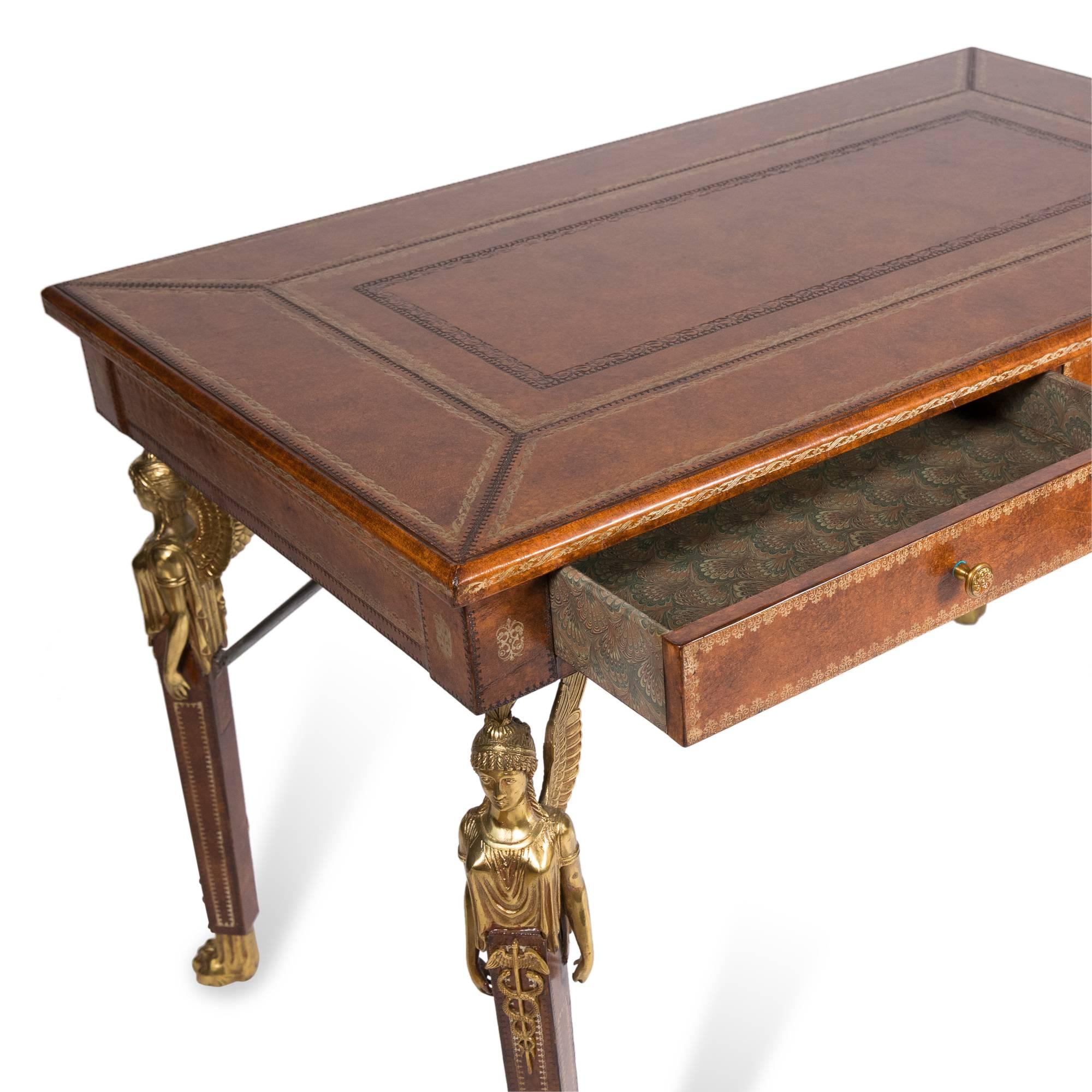 Gilt tooled leather two-drawer desk, with mounted winged solid bronze classical figures on legs, solid bronze paw feet, interior of drawers with scalloped patterned paper lining, by Maitland Smith, United Kingdom 1960s. Measures: Width 43 1/2 in,