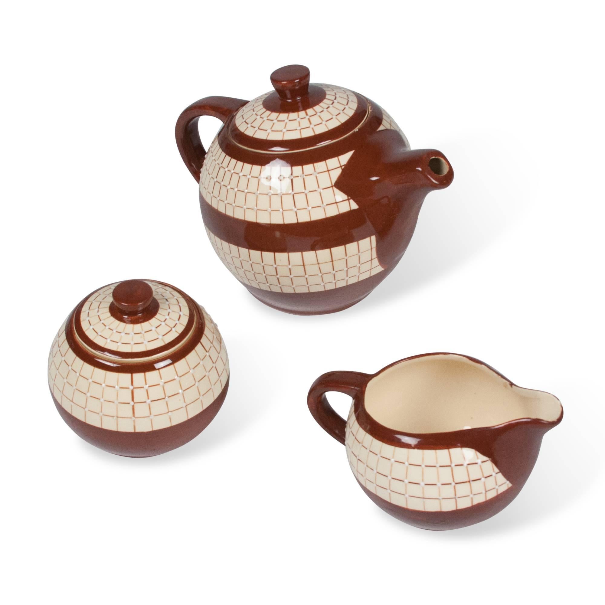 Three-piece ceramic tea service, comprising a tea pot, sugar bowl and creamer, in off-white glaze with red glazed bands, accents, and handles, by Longchamps, France 1950s. Signed to underside. 
Dimensions: 
Teapot: 6 in. height, 5 1/4 in. width, 8