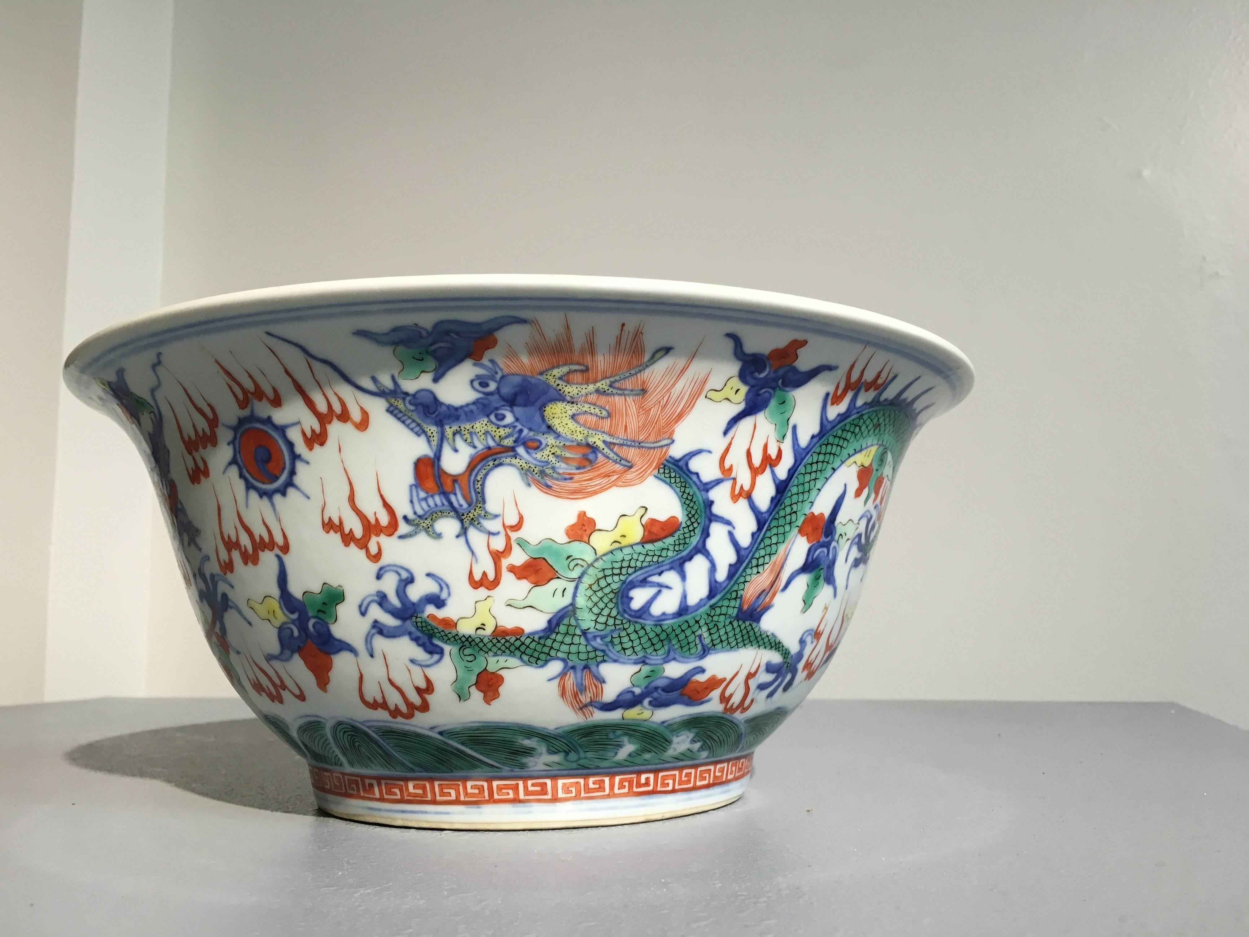 A large Chinese Qing dynasty porcelain wucai (five color) glazed bowl painted in underglaze blue and overglaze red, green, and yellow upon a pure white ground, and featuring a design of dragons to both the exterior and interior. An apocryphal 