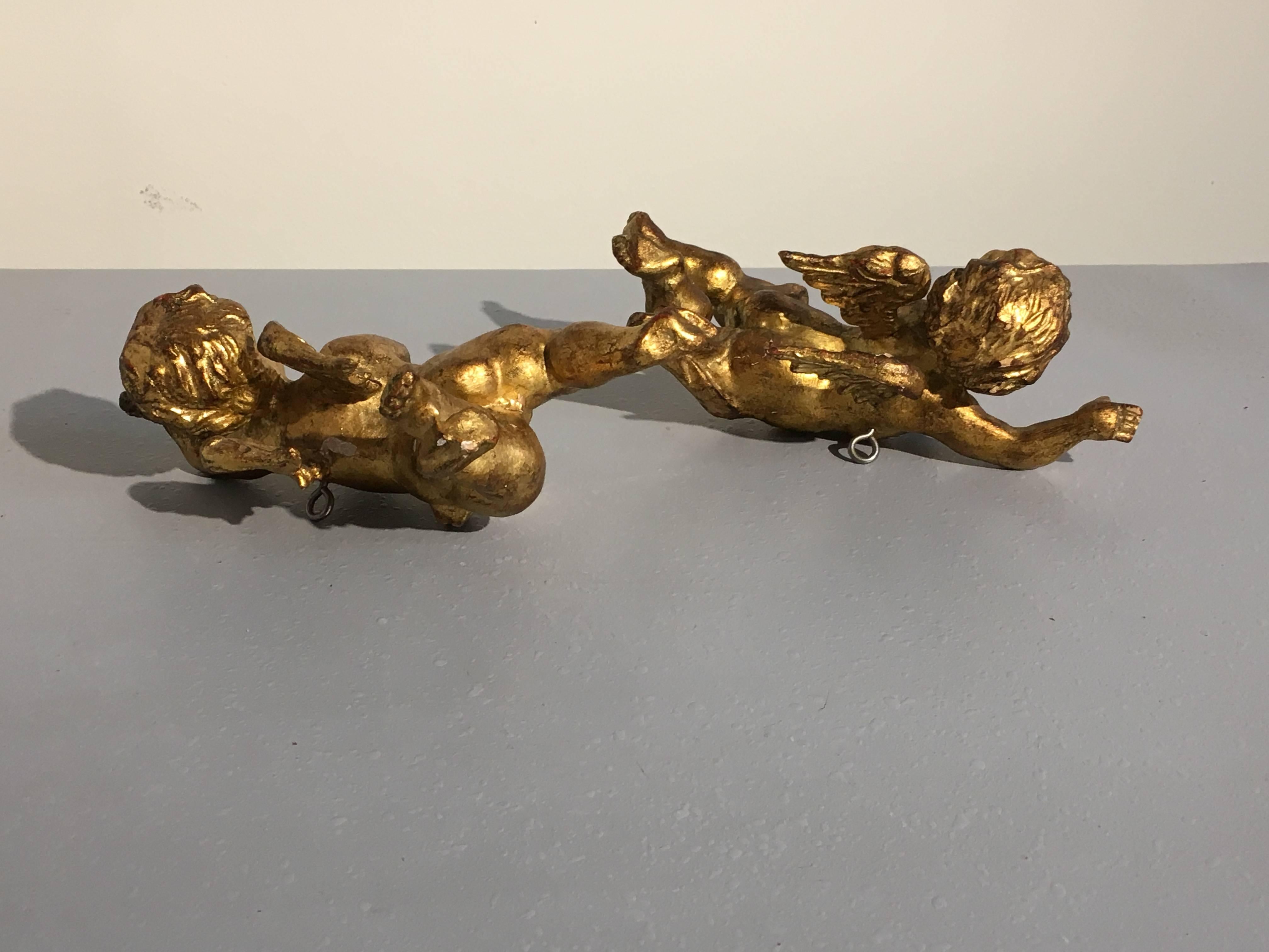 A delightful pair of Italian giltwood putti, or cherubs. The angelic beings carved as chubby, curly haired youths with wings upon their backs. Portrayed as if in flight, arms outstretched, heads turned. 
Fitted with a modern hanging bracket to the