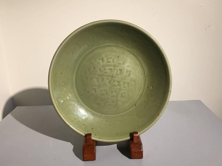 A heavily potted and richly glazed celadon dish, Longquan kilns, early Ming Dynasty, mid 15th century, China. 

The large dish glazed in a deep olive celadon. The interior of the dish with an incised geometric design, similar to a basket weave, but