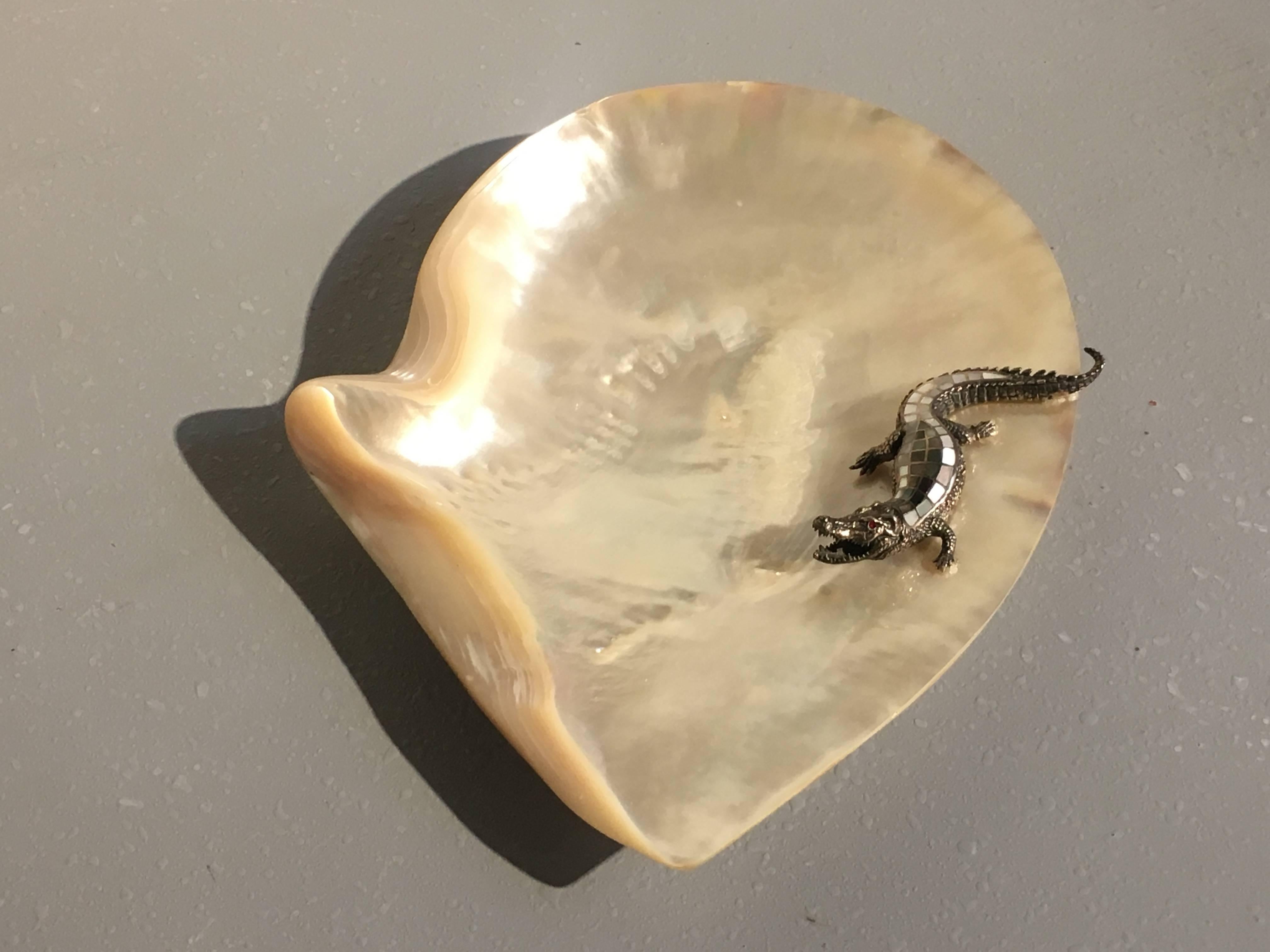 A simply gorgeous mother-of-pearl shell dish. The dish crafted from a single large shell, set upon three mother-of-pearl feet. A silver crocodile with mother-of-pearl scales and red crystal eyes lounges on one side of the dish.
 
