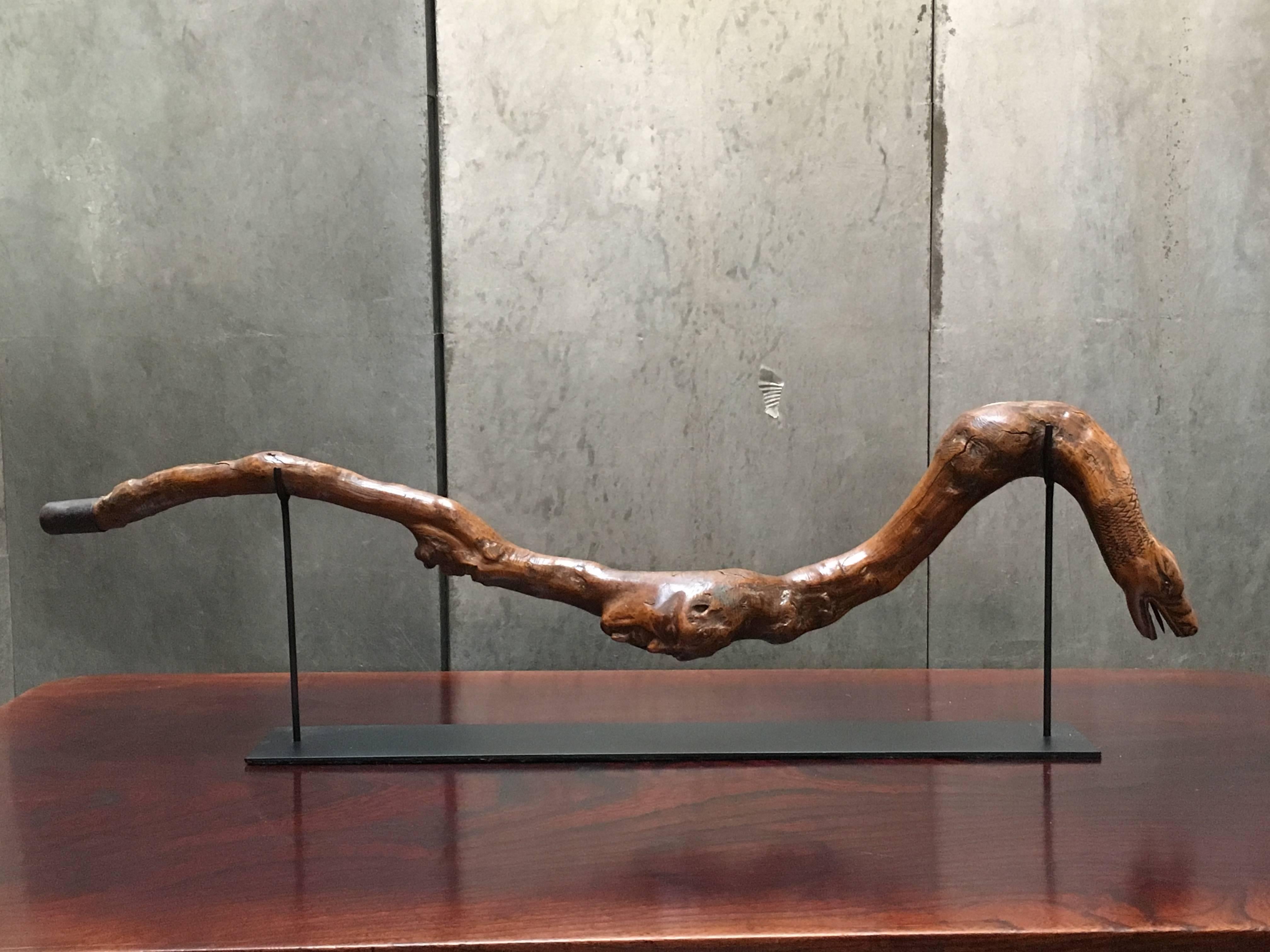 An intriguing early 20th century American folk carved walking stick, mounted as a sculpture.
Carved from a single section of gnarled hardwood in the form of a snake with two wood spirits to the body. The snake head carved masterfully with an open
