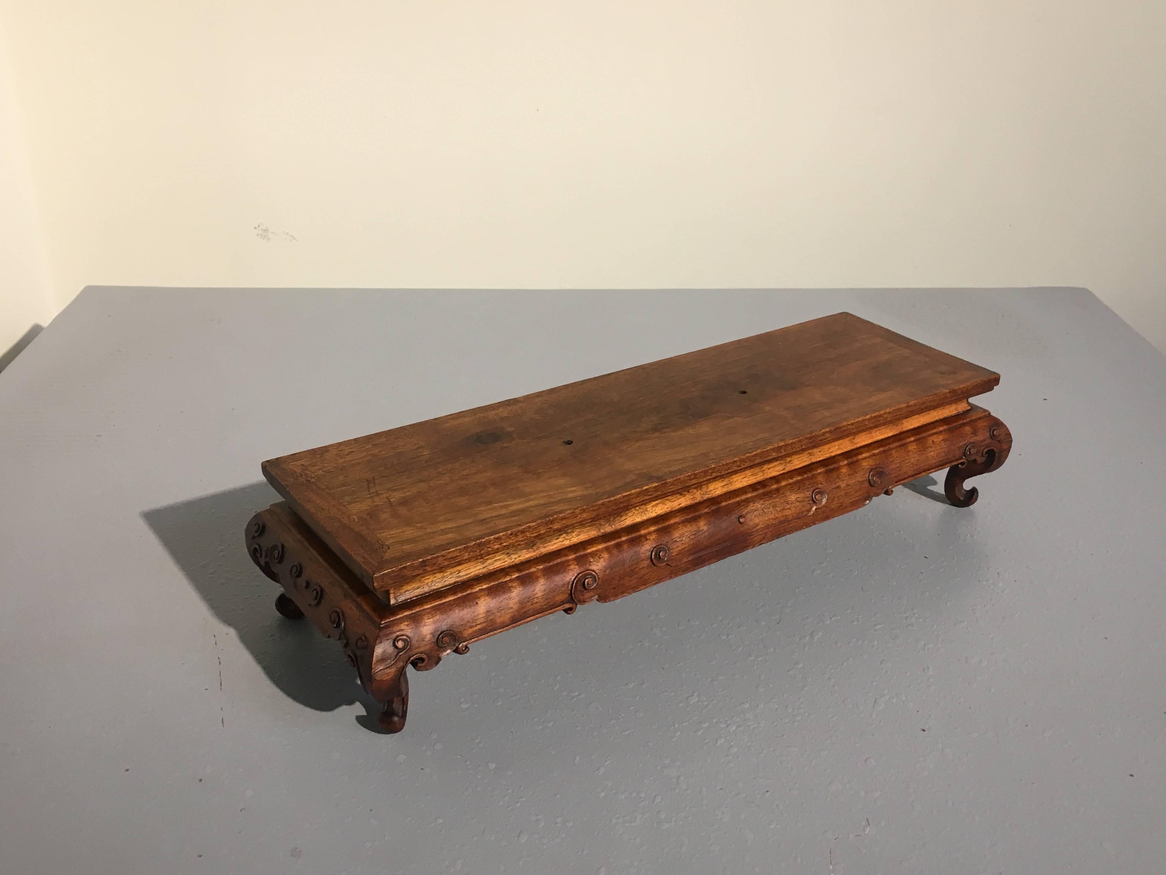 A truly gorgeous Chinese huanghuali wood display stand in the form of a table. 
The single plank top with edge molding featuring an attractive grain and rich luster. A narrow waist sits above a shaped apron carved in low relief with stylized ruyi.