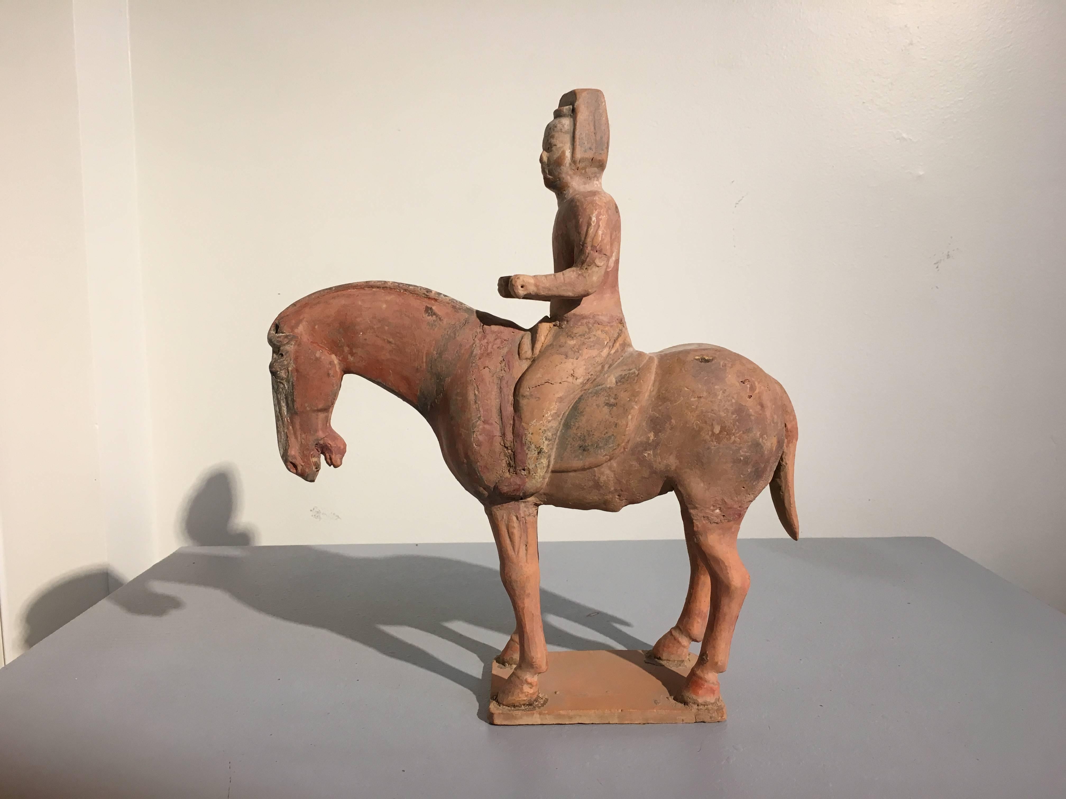 Charmante figurine en poterie peinte de la dynastie Tang représentant un cheval et son cavalier noble. TL testé par Oxford Authentication. 
Le cheval est représenté debout, la tête baissée et détendu. Le cavalier est assis droit sur sa selle, la