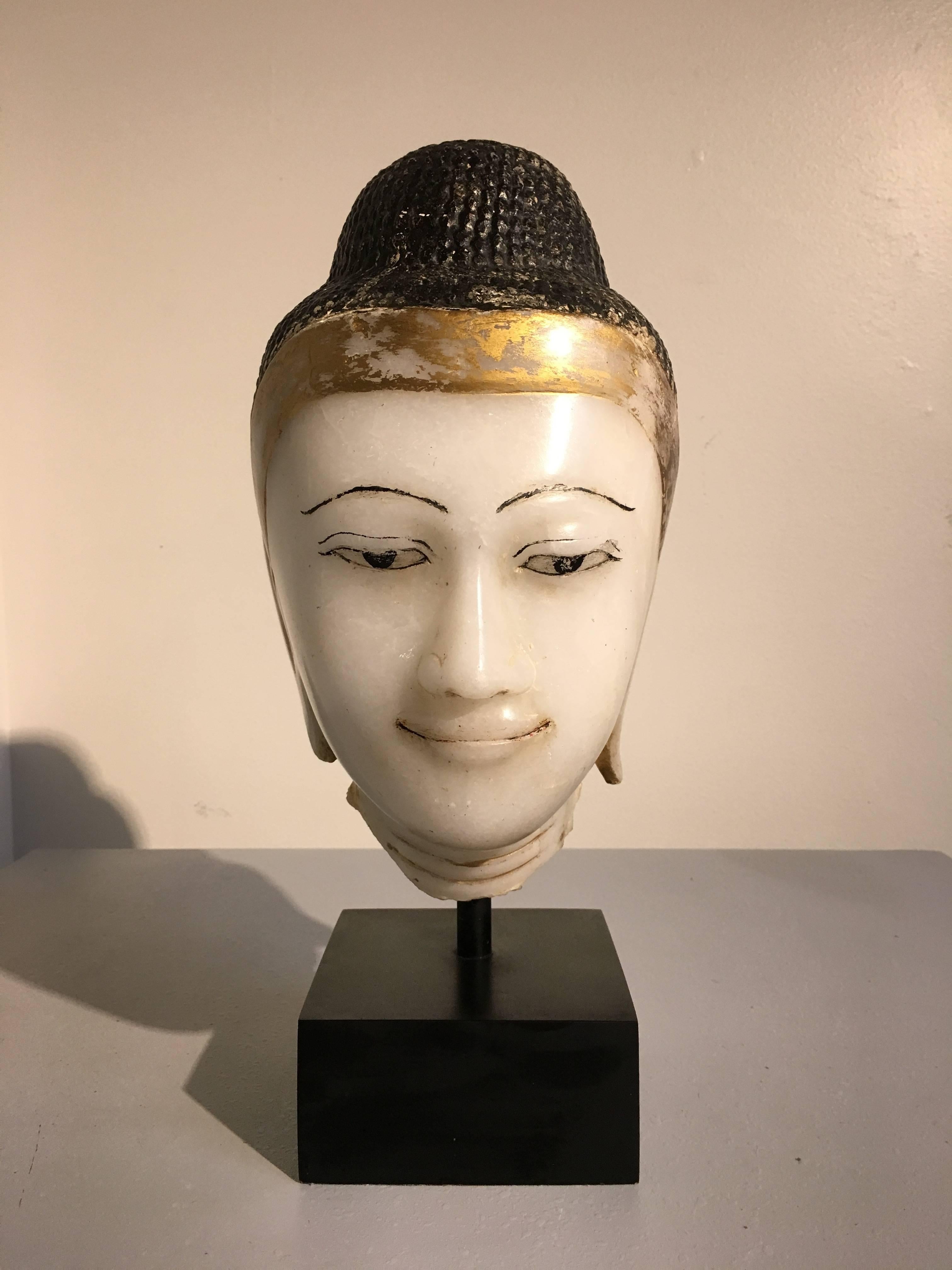 A sublime Burmese carved and painted alabaster head of the Buddha, Mandalay Period, early 19th century. 
The face of the Buddha has been beautifully rendered in a milky white alabaster with flecks of mica that catch the light. The features of his